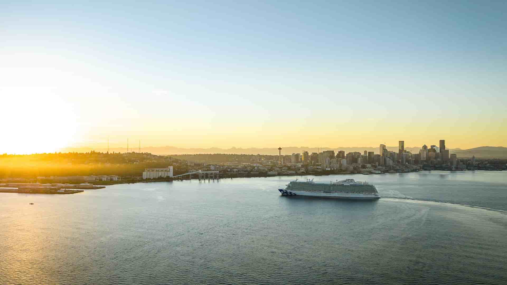 The Discovery Princess cruise ship sailing past the Seattle skyline at sunset, with the Space Needle visible in the background.