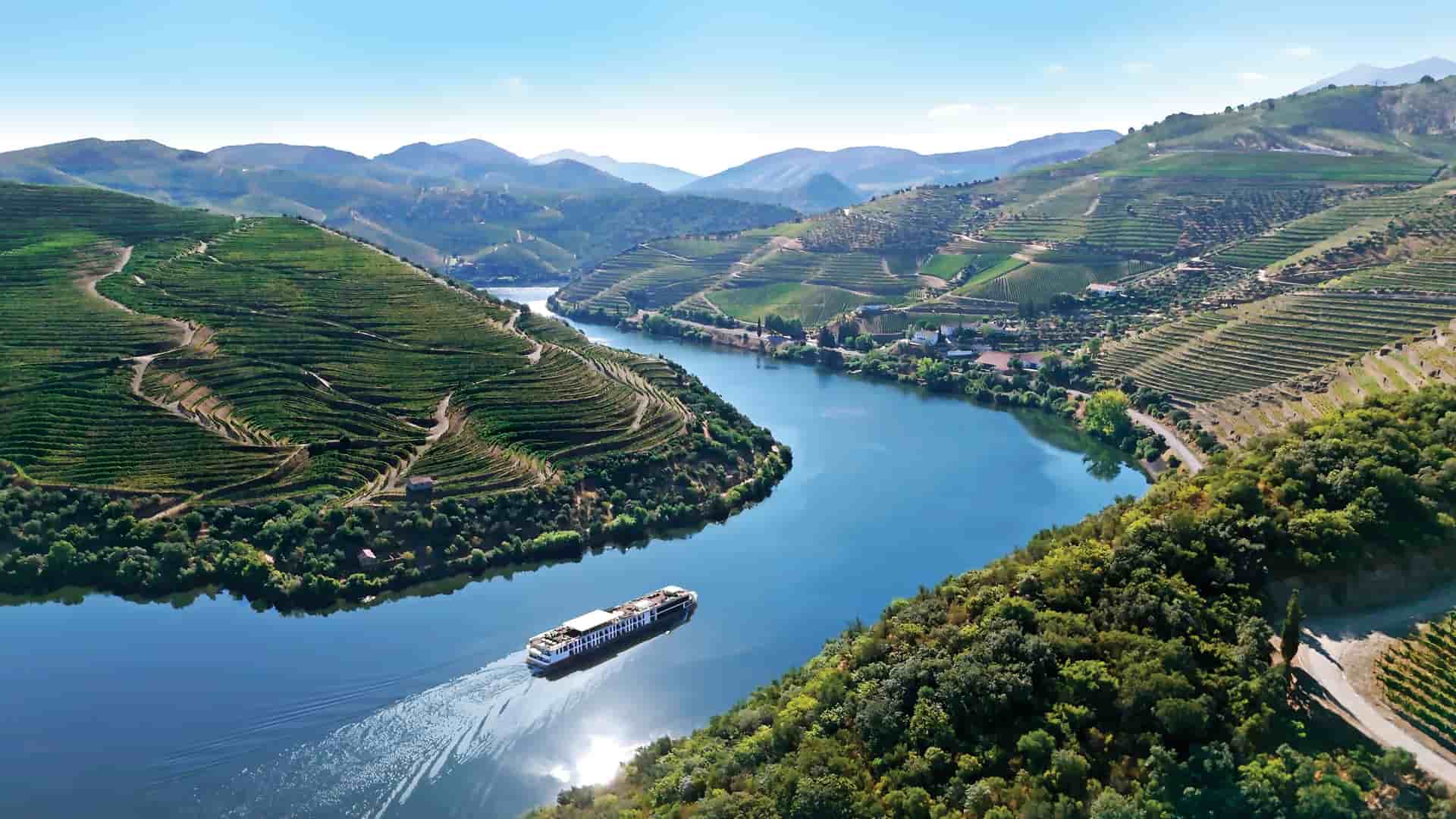 The AmaWaterways AmaVida river cruise ship sailing through the scenic Douro River Valley in Portugal, with picturesque terraced vineyards covering the hillsides.