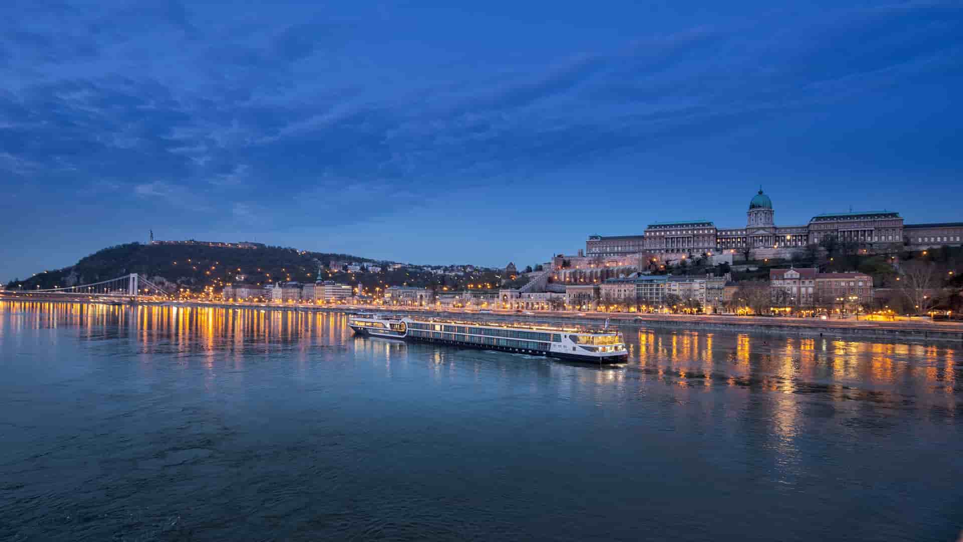   Avalon Waterways river cruise ship on the Danube River at twilight in Budapest, Hungary, with illuminated buildings and reflections.
