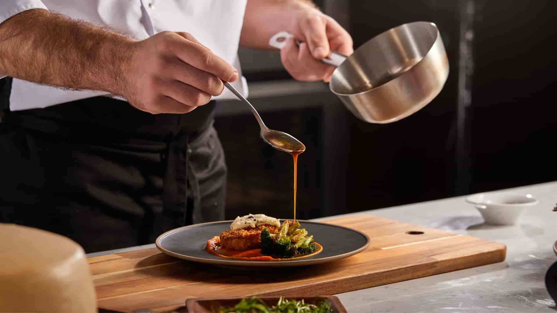 A chef drizzling a sauce on a plated meal before serving to restaurant guests.