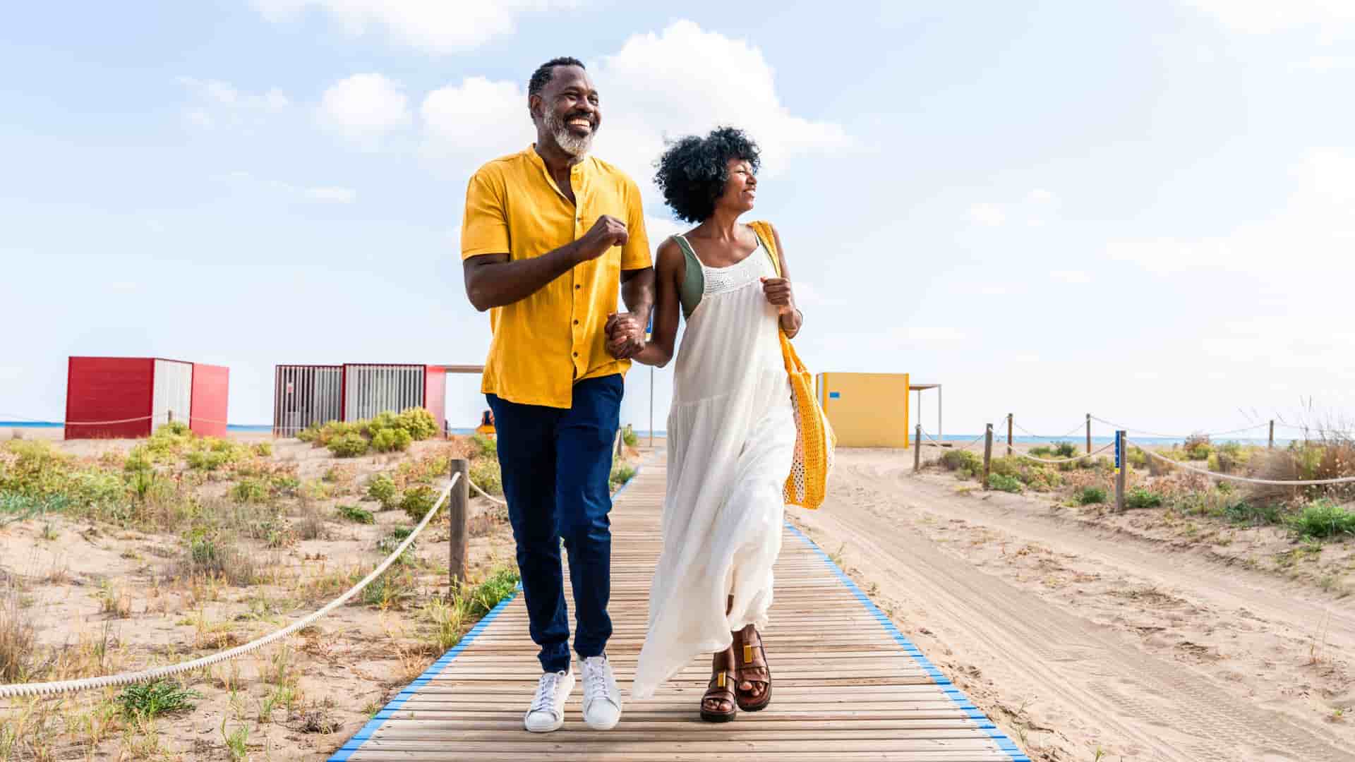A happy couple holding hands while walking down a beach baordwalk during a cruise excursion. 