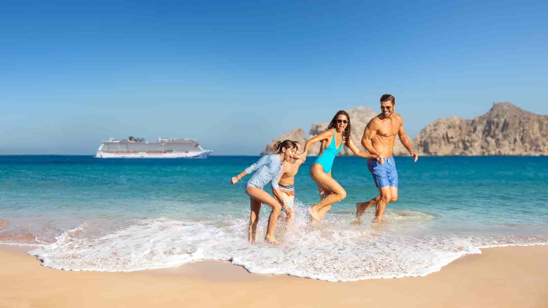 A family enjoys a fun beach day in Cabo San Lucas, Mexico, with a Norwegian Cruise Line ship sailing in the background on a Mexican Riviera cruise.
