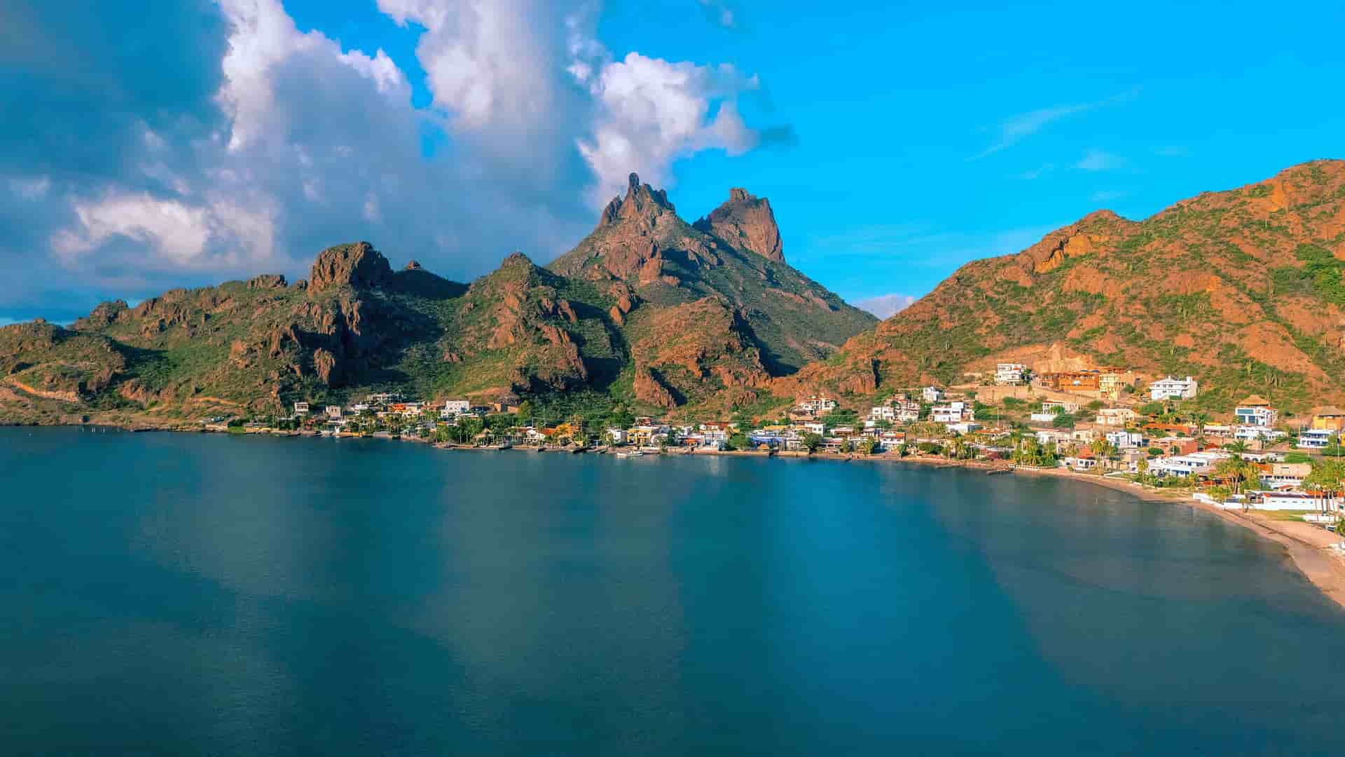 An aerial view of the scenic bay and coastal community in Guaymas, Mexico, with rugged mountains and a beautiful blue sky in the background.
