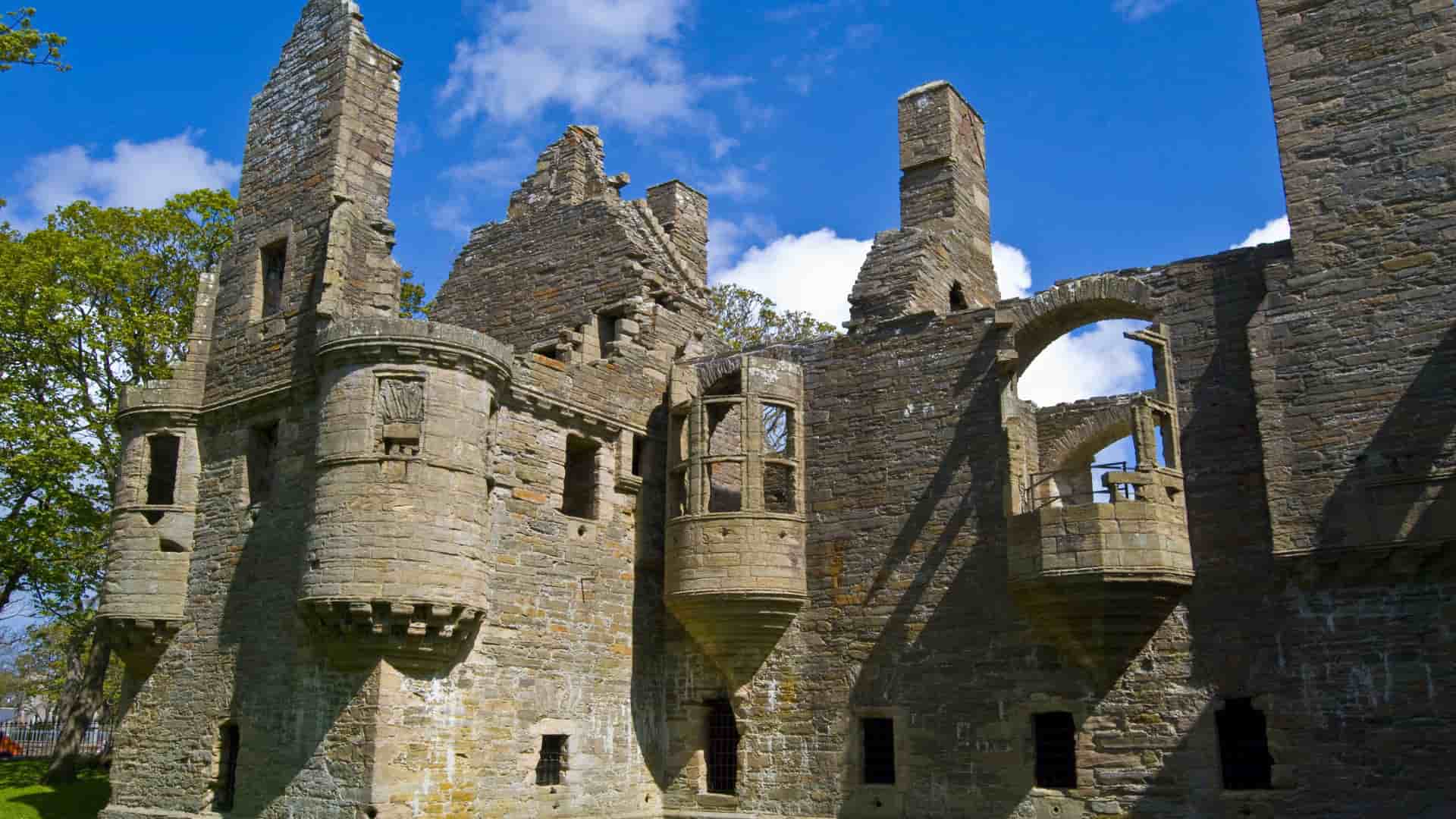 The impressive stone ruins of the Earl's Palace, a historic landmark in Kirkwall on the Orkney Islands, with detailed stonework and arches under a bright blue sky.