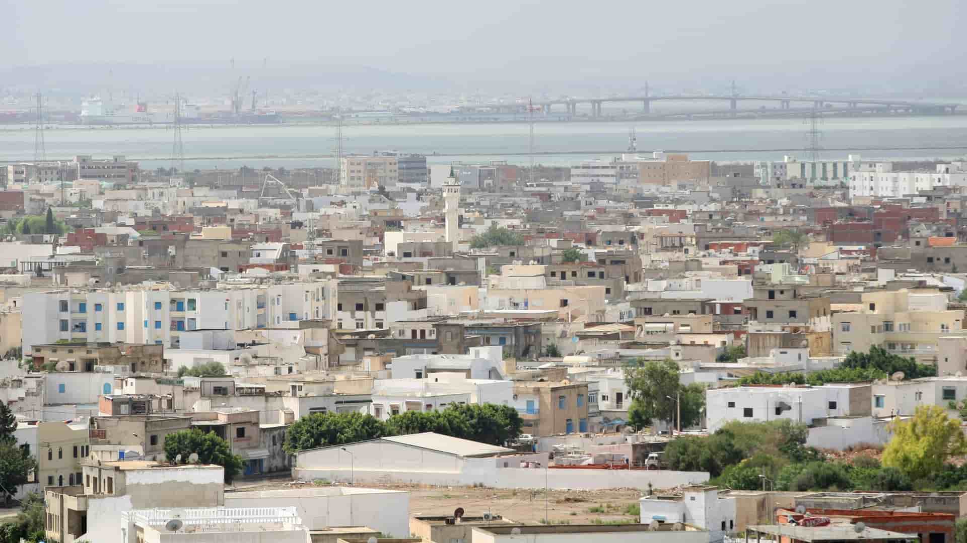 An extensive aerial shot of the port city of La Goulette, Tunisia, with dense white buildings and a central minaret, a vibrant urban landscape on the Mediterranean coast.