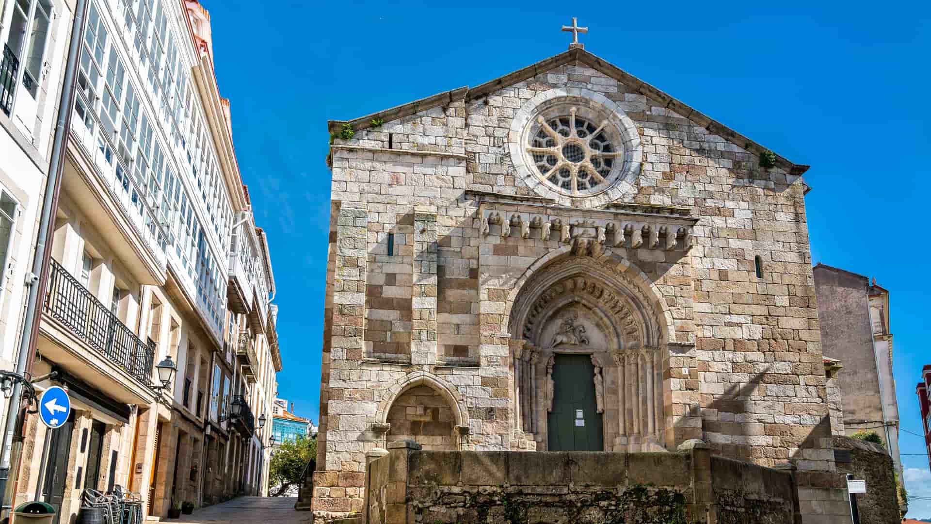 "A low-angle view of the historic Romanesque Church of Santa Maria de Fisterra in Lestedo, Spain, featuring its stone facade, arched entrance, and a rose window.  "
