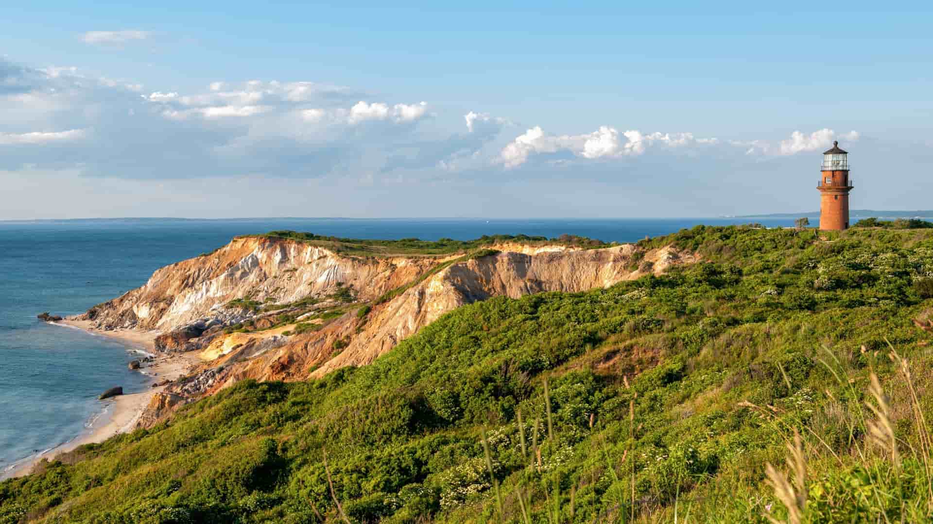 A picturesque view of a brick lighthouse perched on the lush, green cliffs of Maroe Bay, Huahine, with the ocean and a blue sky in the background.