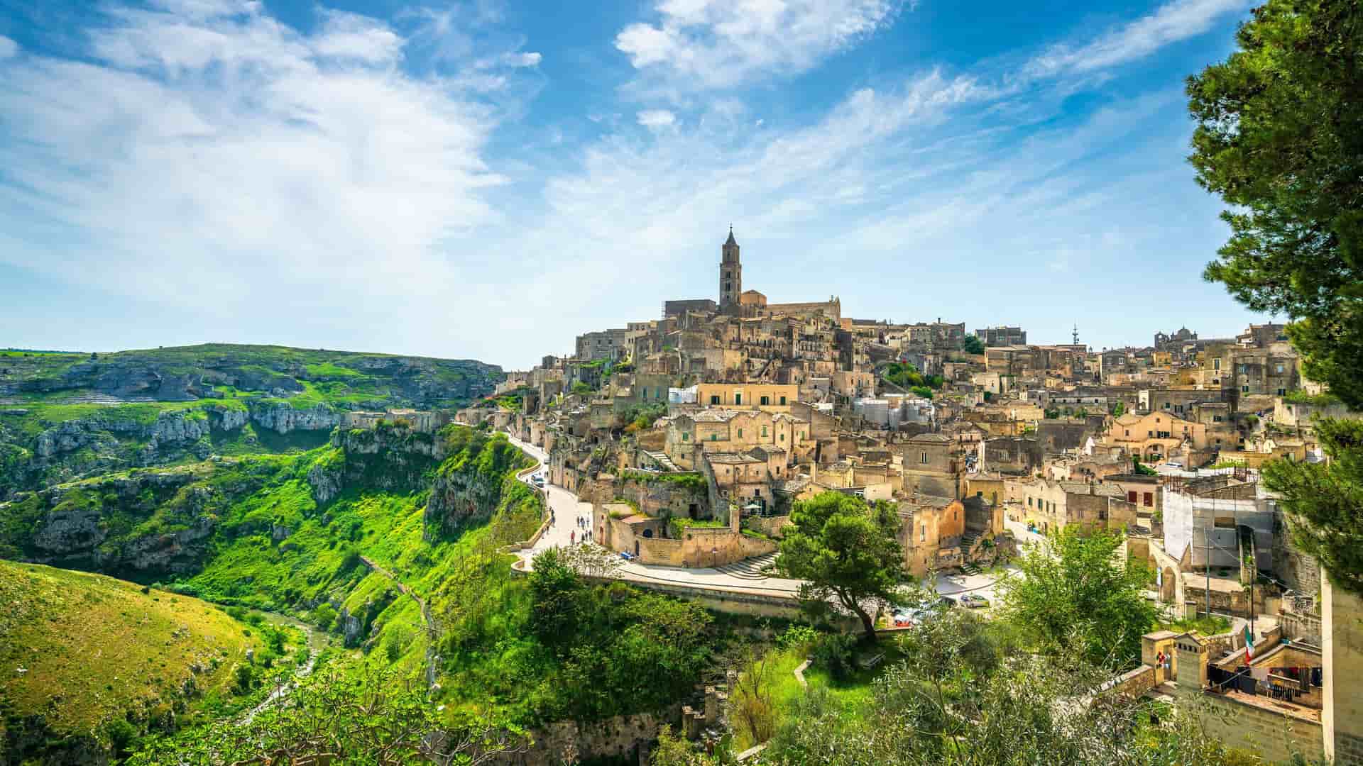 "A stunning panoramic view of the ancient Sassi di Matera cave dwellings in Matera, Italy, with the historic city perched on a hillside and a deep gorge beside it.  "