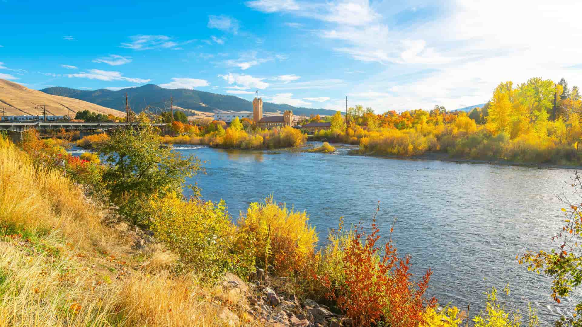 "A stunning autumn view of the Clark Fork River in Missoula, Montana, with the historic Milwaukee Depot in the background and vibrant yellow foliage along the riverbank.  "