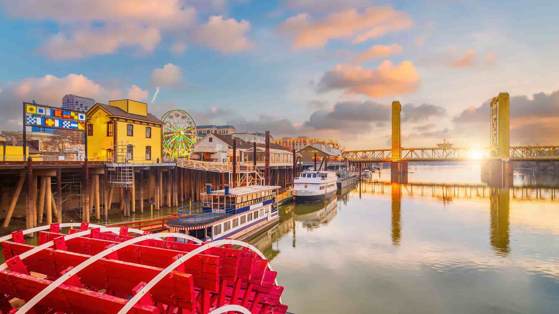 "A picturesque sunset view of Old Sacramento, California, with the iconic Tower Bridge and riverboats on the Sacramento River, a popular tourist destination.  "