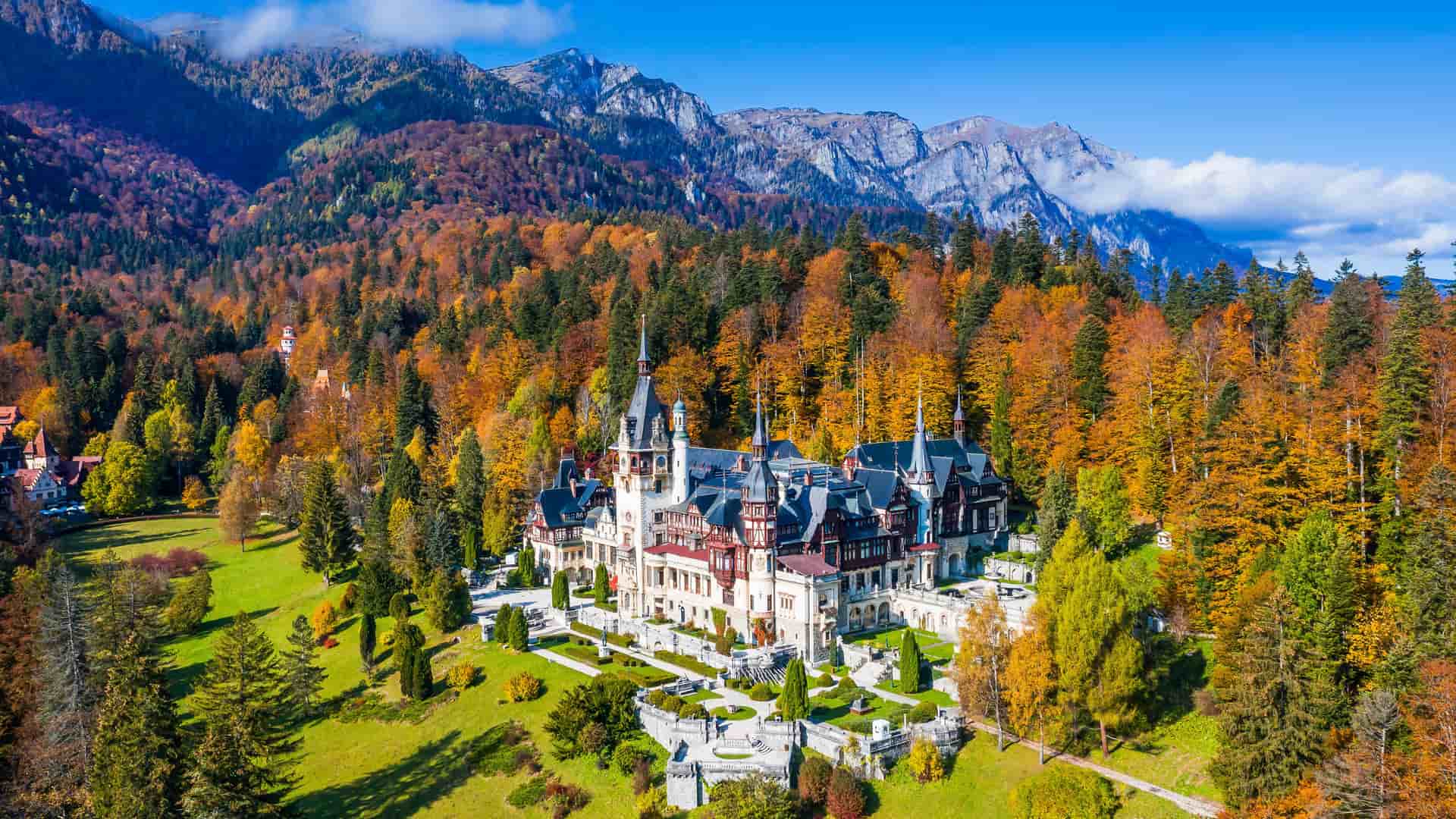 A high-angle view of the beautiful Peleș Castle in Sinaia, Romania, a neo-renaissance building nestled in the Carpathian Mountains, surrounded by lush autumn foliage and gardens.
