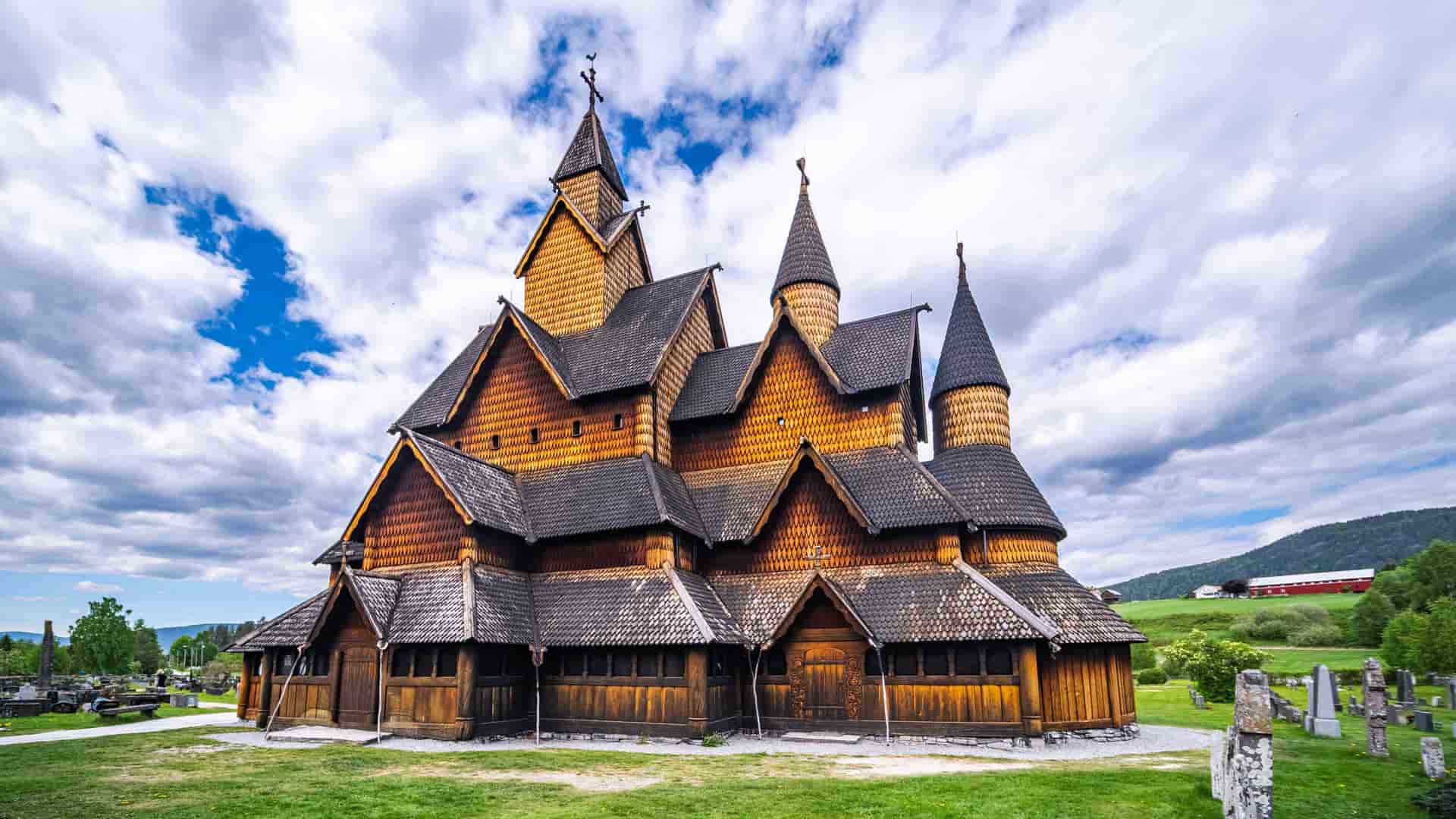 "A beautiful wide-angle shot of the medieval Heddal Stave Church, a unique and historic wooden structure with multiple roofs and spires, surrounded by a green lawn and a cemetery in Telemark, Norway.  "