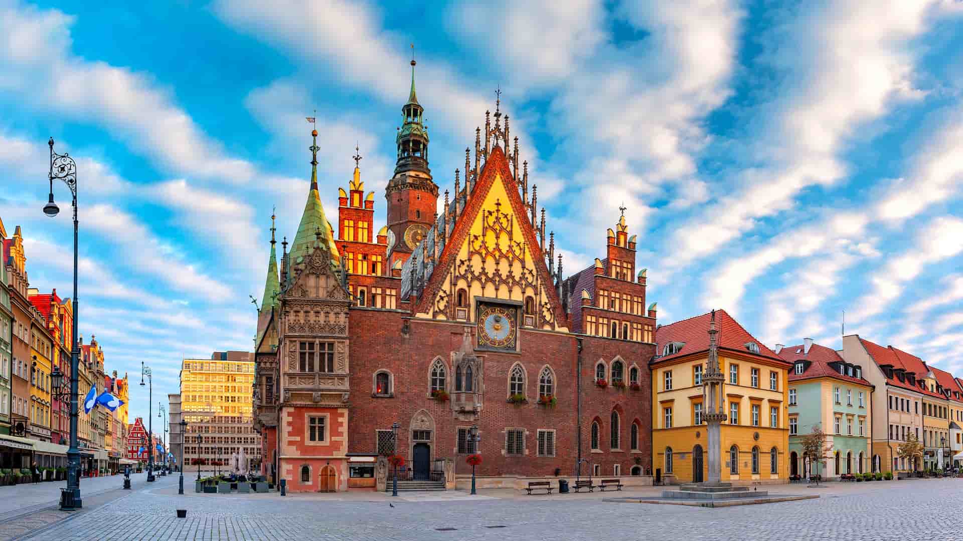 "A vibrant panoramic shot of the historic Wroclaw Old Town Hall in Poland, with its intricate gothic architecture and clock tower, surrounded by a cobblestone square."