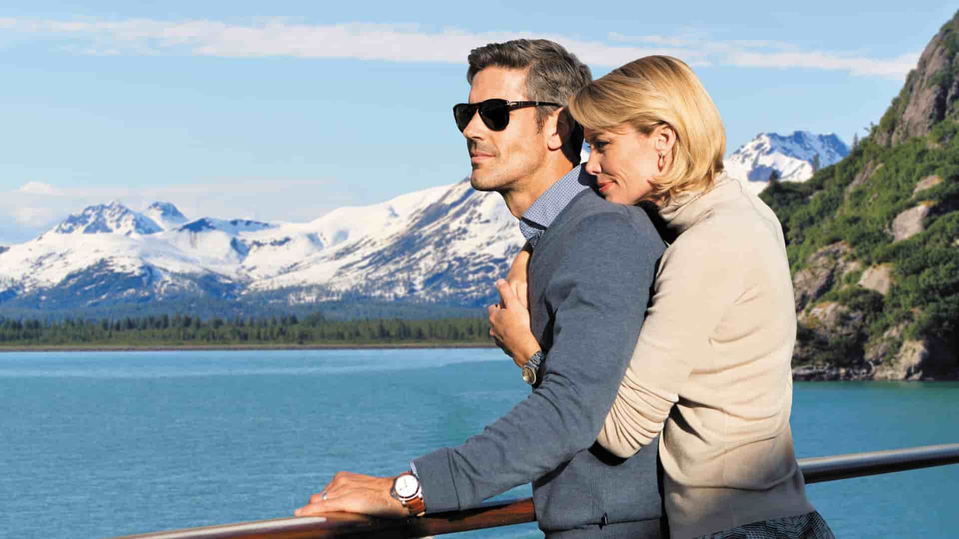 A happy couple standing leaning on the railing of the ship on a luxurious and romantic Regent Seven Seas Alaskan cruise.