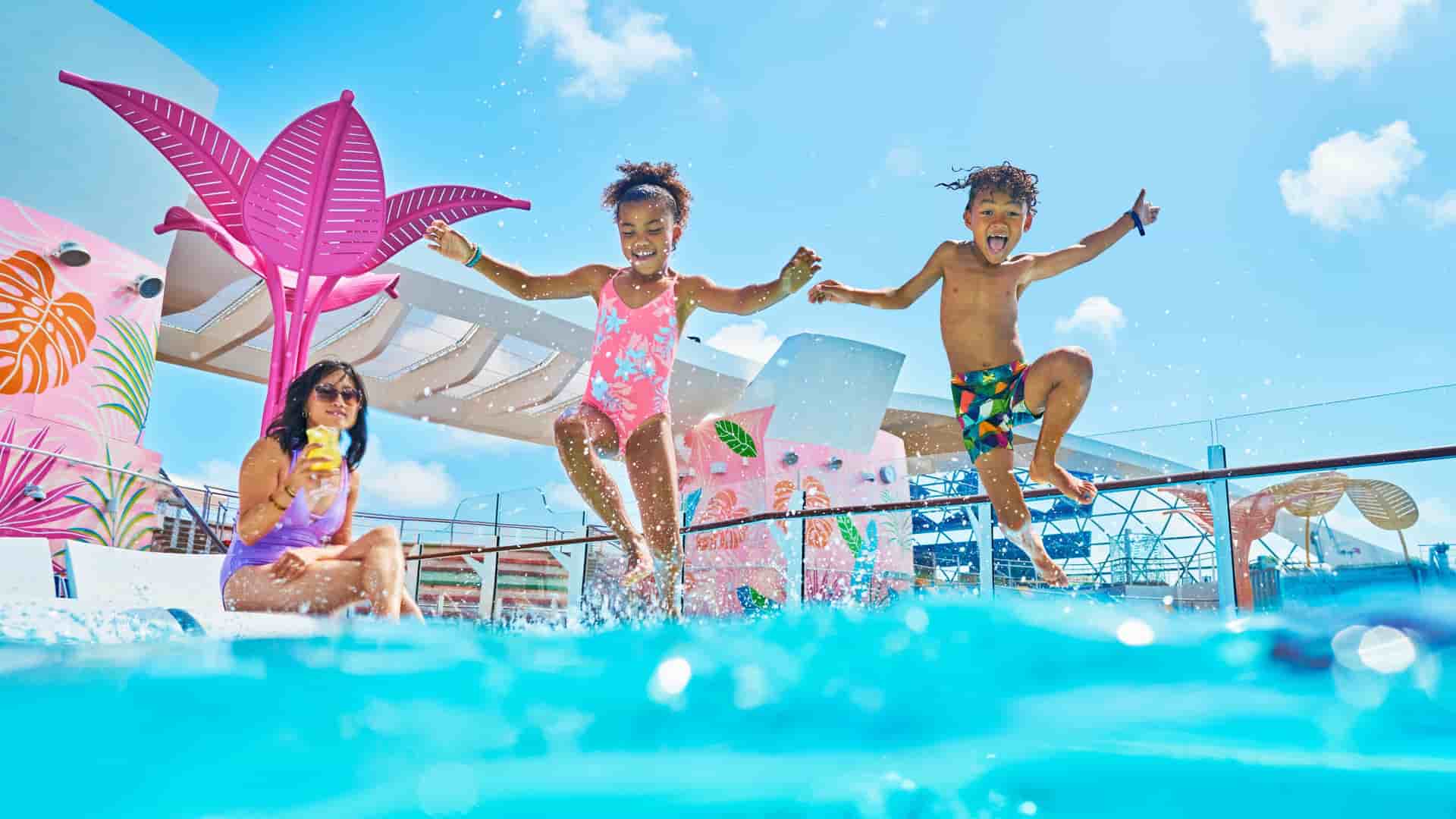 Two children joyfully jump into a vibrant pool on a Royal Caribbean cruise ship's deck, with a colorful water feature in the background.