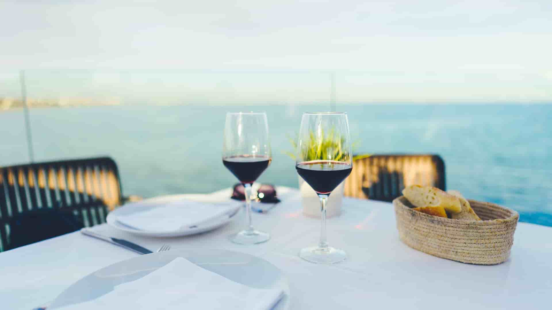 Two glasses of wine on a table with the ocean in the background.