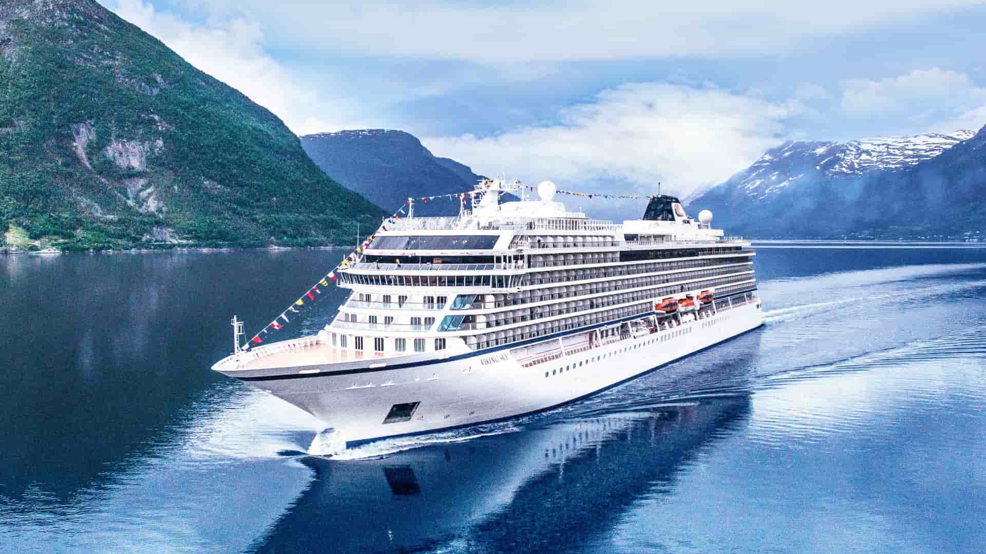 A Viking Ocean cruise ship sails through the waters of Eidfjord, a stunning Norwegian fjord surrounded by lush, green mountains.