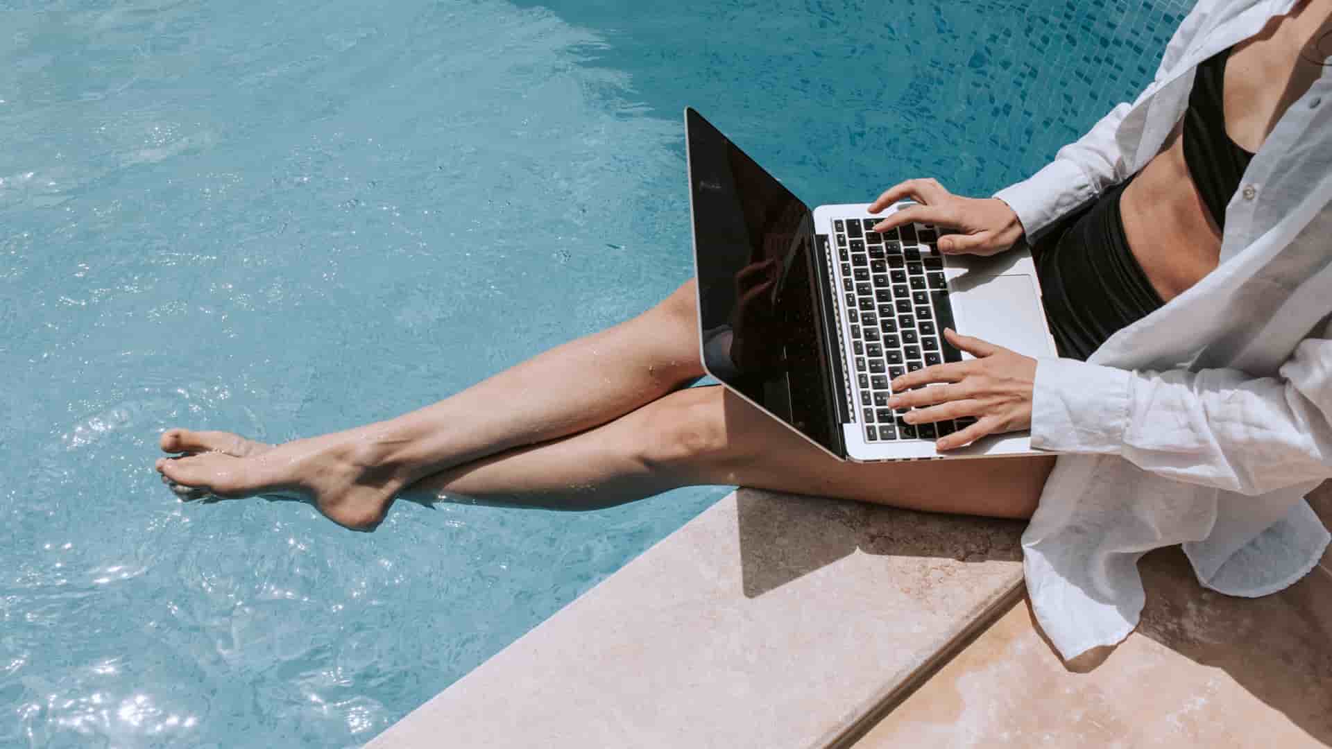 A woman sitting poolside utilizing the cruise ship's Wi-Fi to surf the web on her laptop.