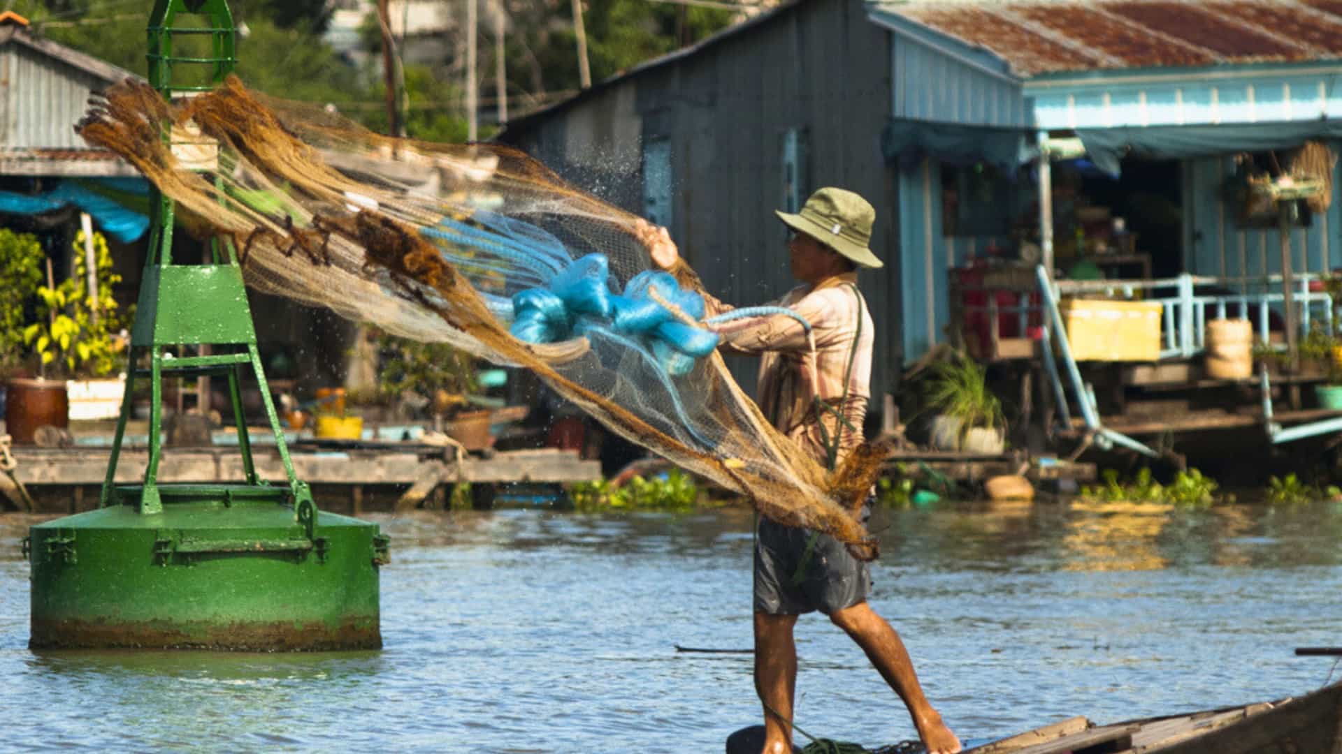 A fisherman casts his net on an Asian river, the Mekong Delta in Chau Doc, Vietnam, showcasing local life and experiences offered on an Avalon Waterways cruise.