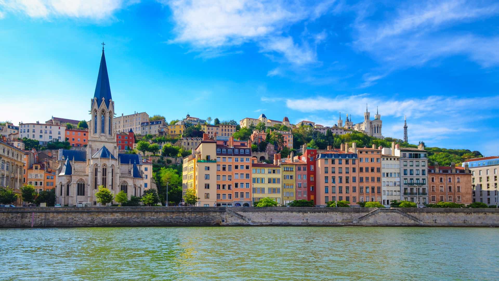 Vibrant cityscape of Lyon, France, with historic buildings and prominent churches lining the Saône riverbank under a bright sky, a cultural highlight on an Avalon Waterways river cruise.