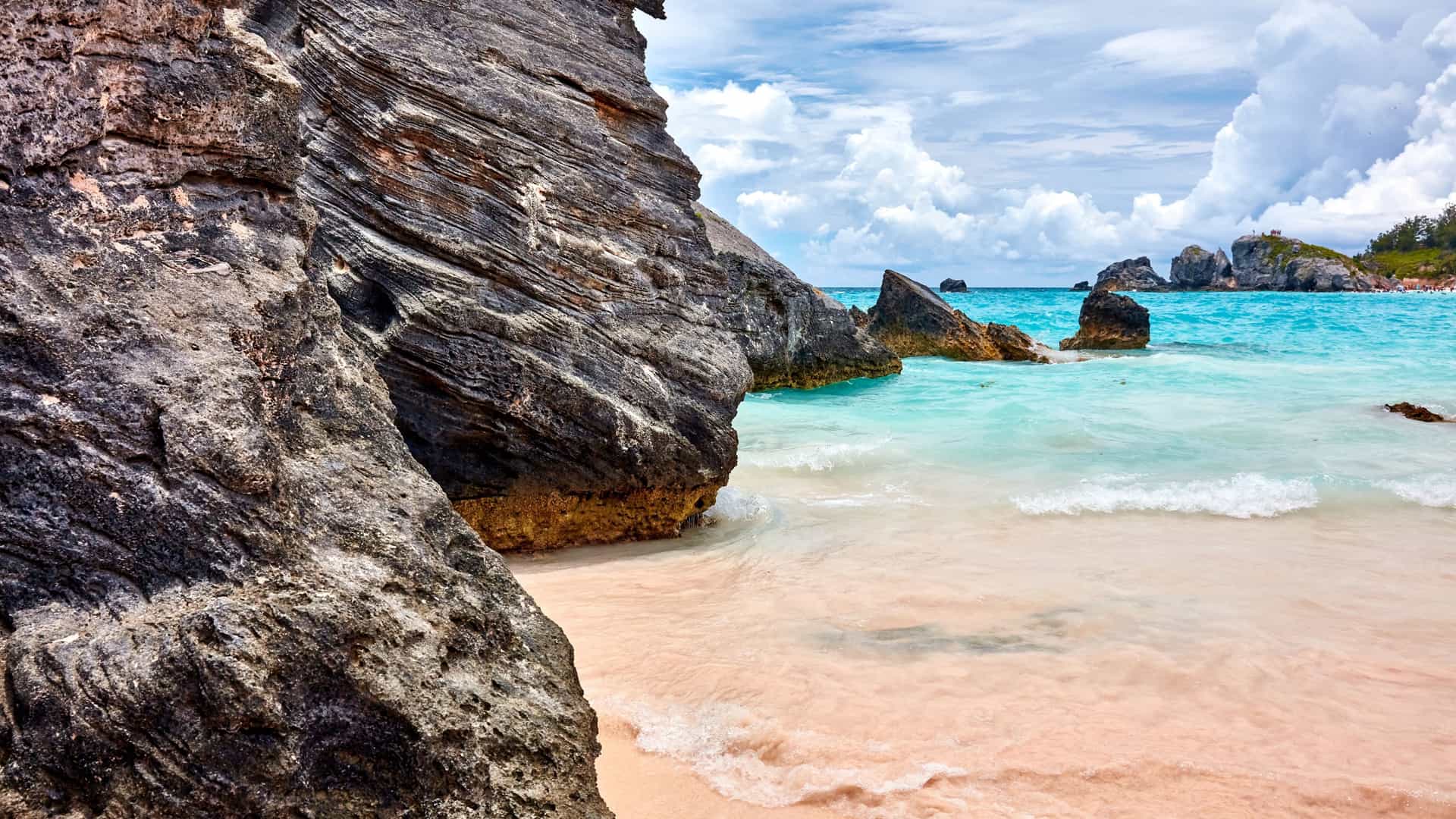 A beautiful pink sand beach with turquoise water and dramatic rock formations in Bermuda, a scenic highlight for Azamara Cruises.