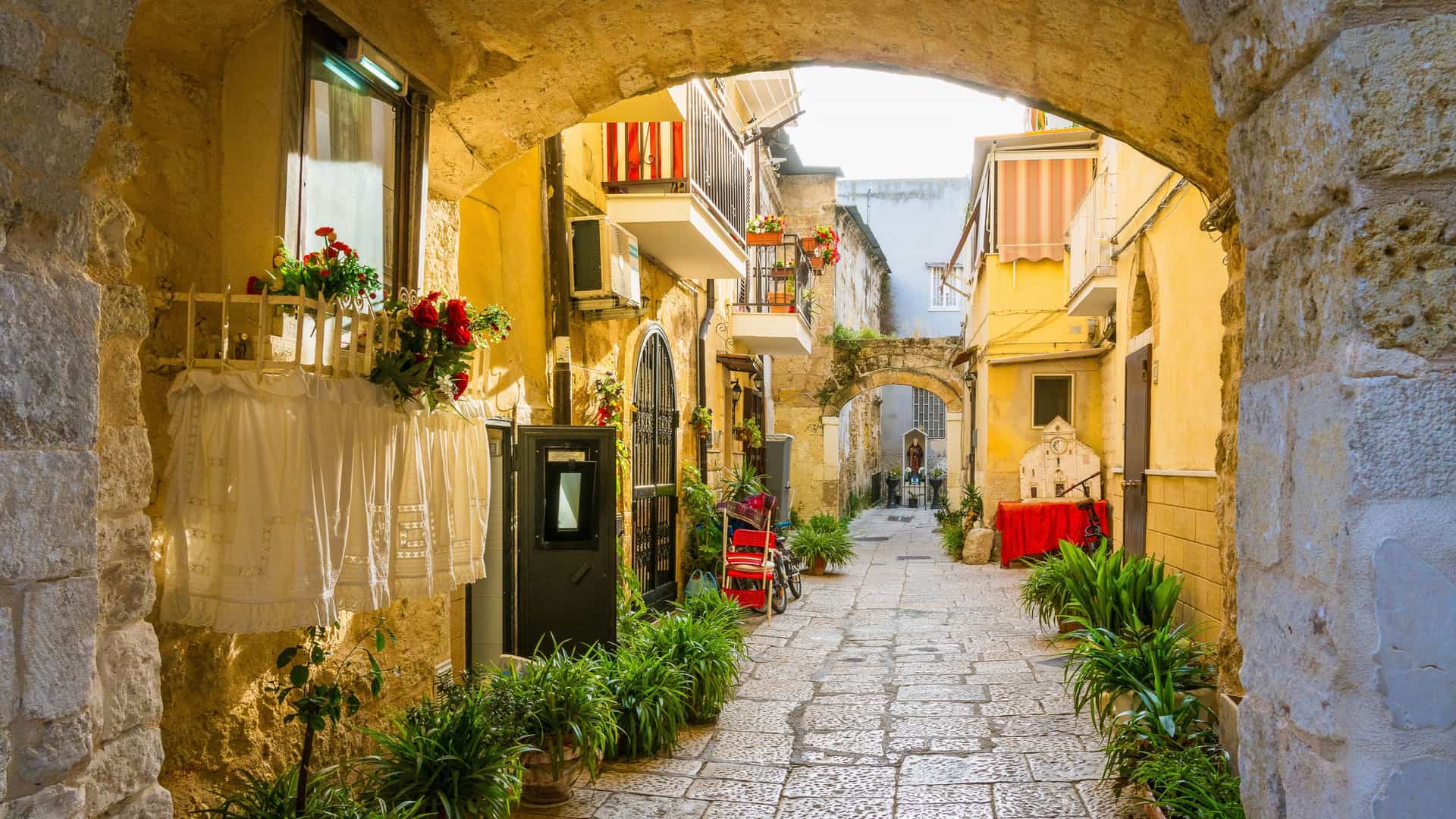 A scenic sight in the Old Town of Bari (Bari Vecchia), Puglia, Italy, featuring a narrow, arched street with laundry hanging between the historic buildings.