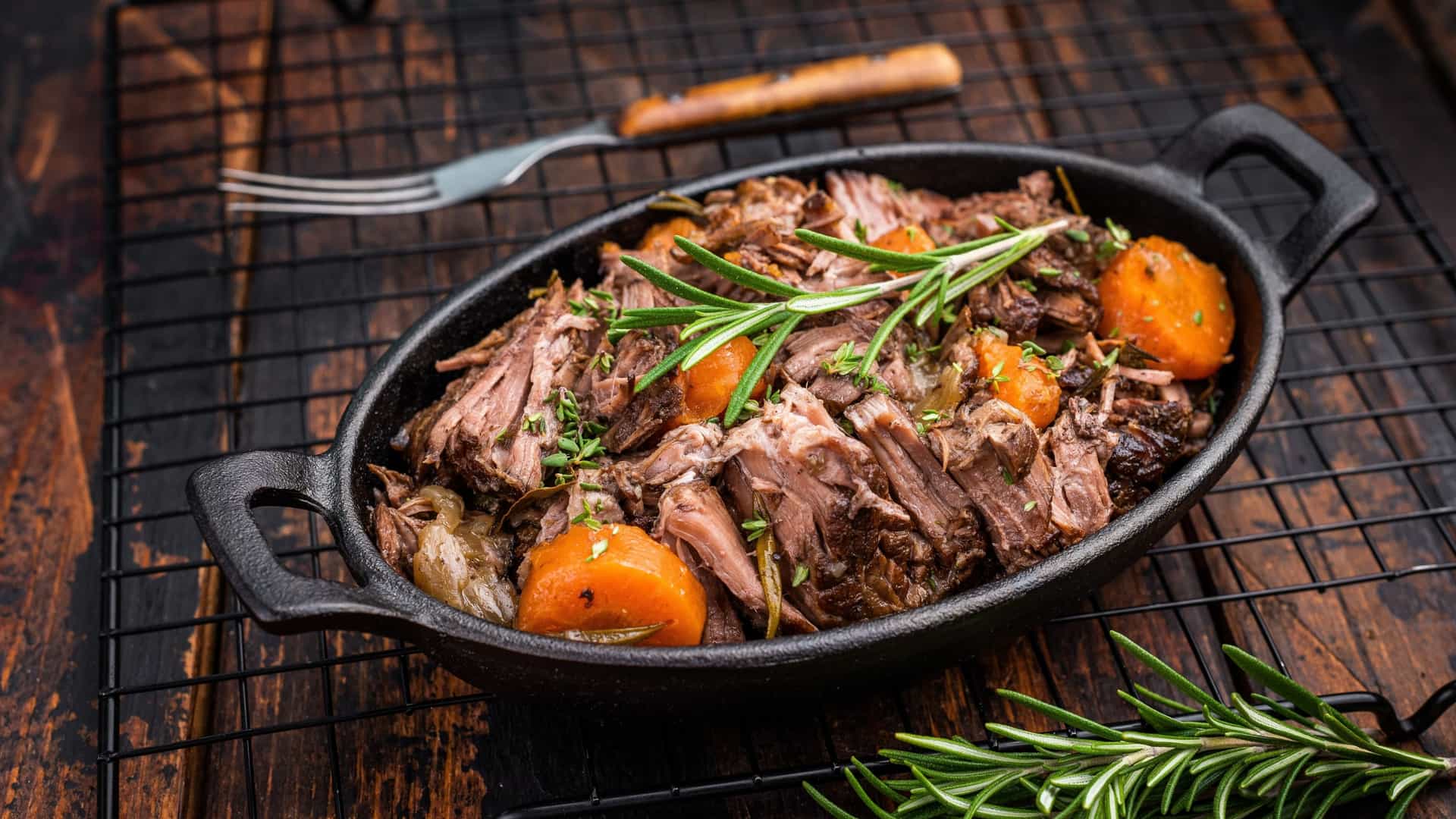 A skillet of beef bourguignon with tender carrots, mushrooms, and potatoes, garnished with fresh parsley.