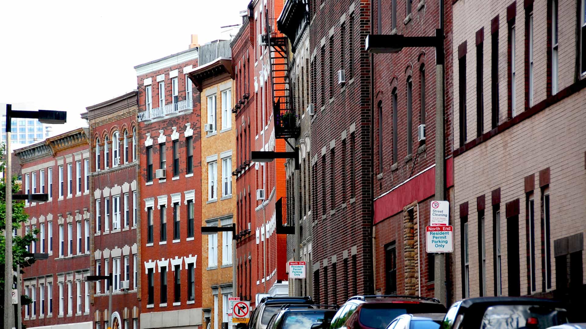 A narrow, cobblestone street in the North End of Boston, Massachusetts, featuring historic brick buildings and streetlights, typical of the city's historical district.