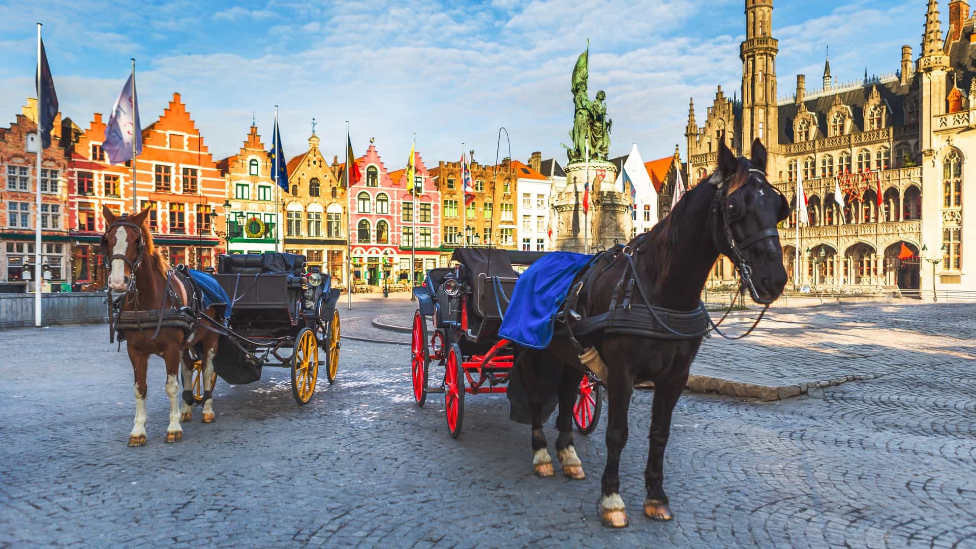 The Grote Markt (Market Square) in Bruges, Belgium, featuring historic guildhalls, the Belfry of Bruges, and several horse-drawn carriages waiting for riders.