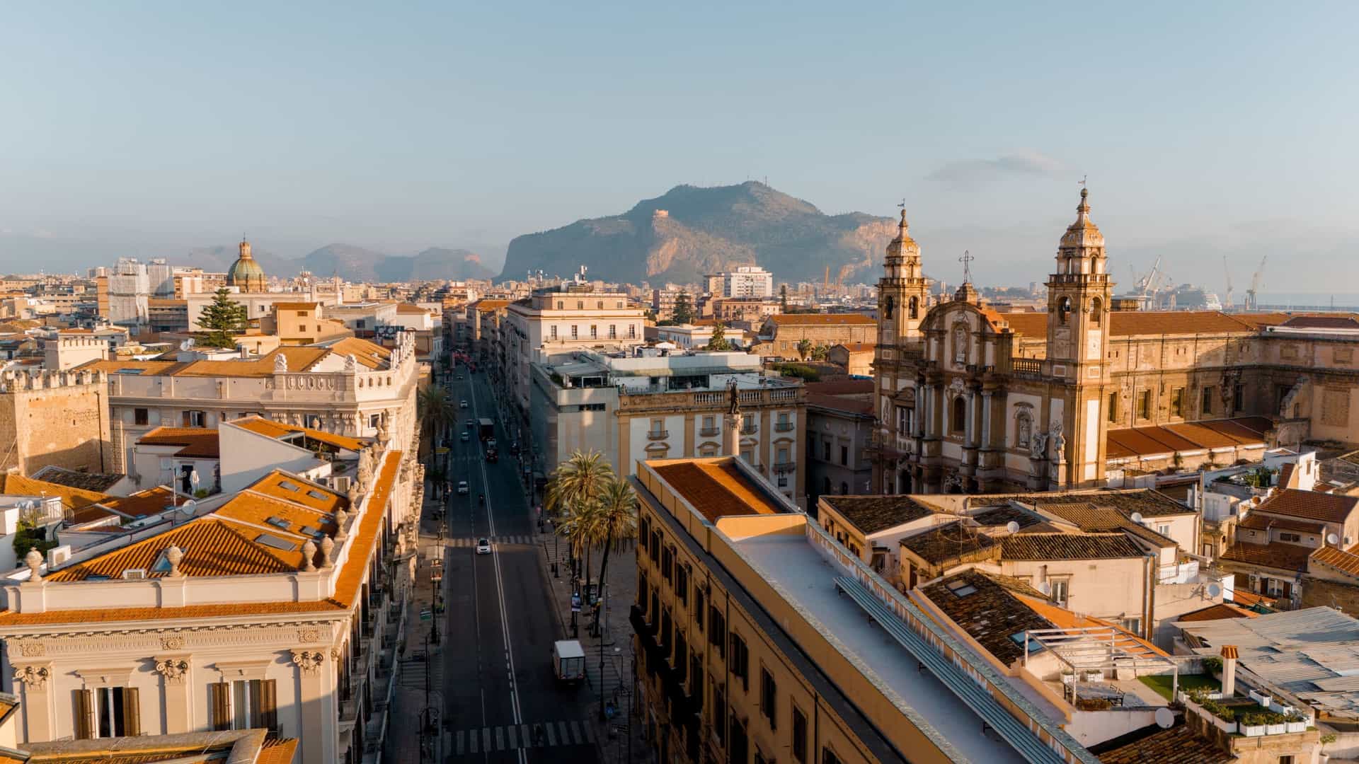 An aerial view looking down Via Roma in Palermo, Sicily, Italy, showing the wide street bustling with traffic, flanked by large, multi-story historic buildings with ornate facades.
