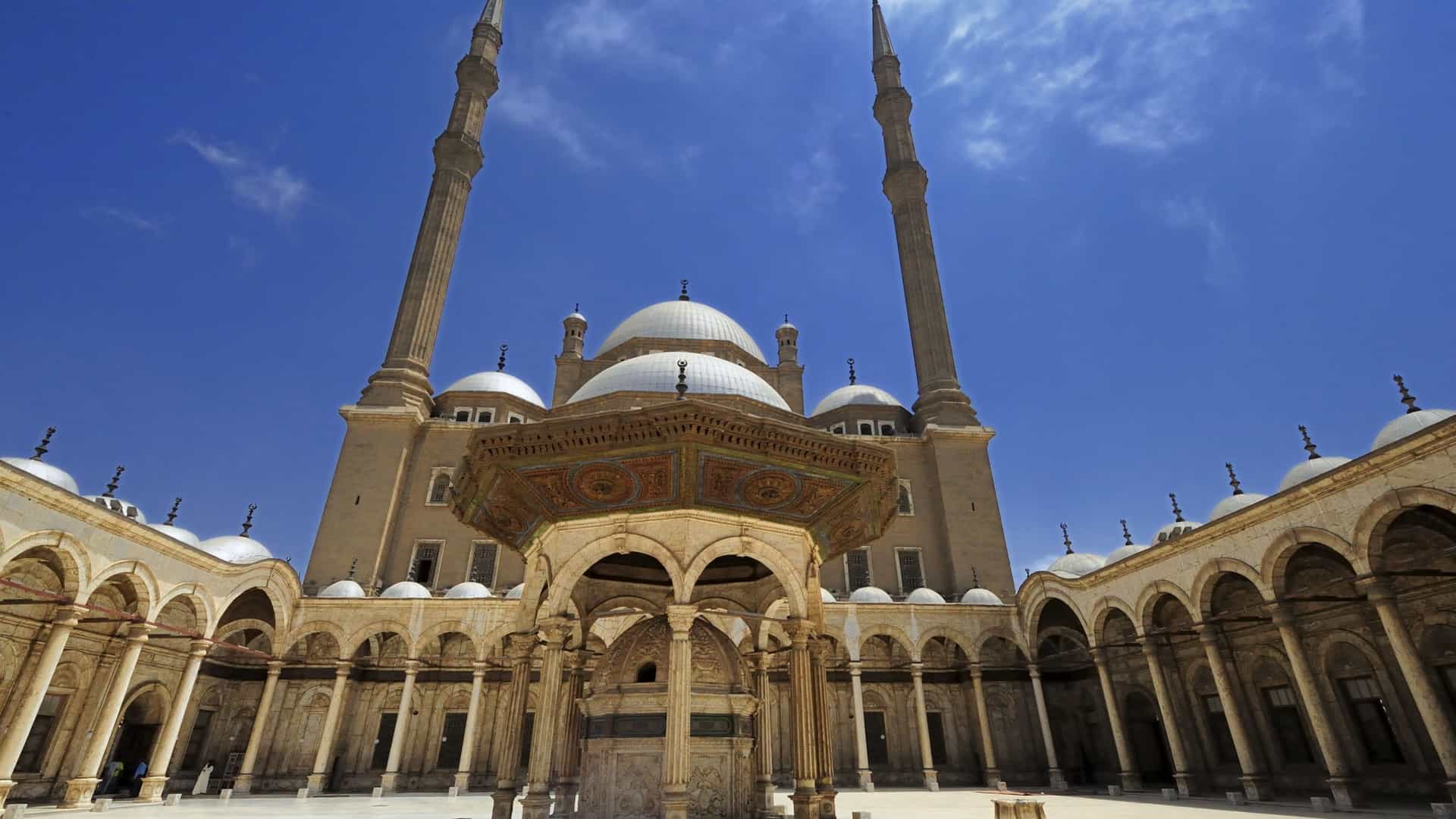  The exterior of the Mosque of Muhammad Ali, also known as the Alabaster Mosque, in Cairo, Egypt. The mosque, situated within the Citadel of Cairo, features a large central dome, several smaller domes, and two prominent Ottoman style minarets. It is constructed from alabaster, giving it a bright appearance.