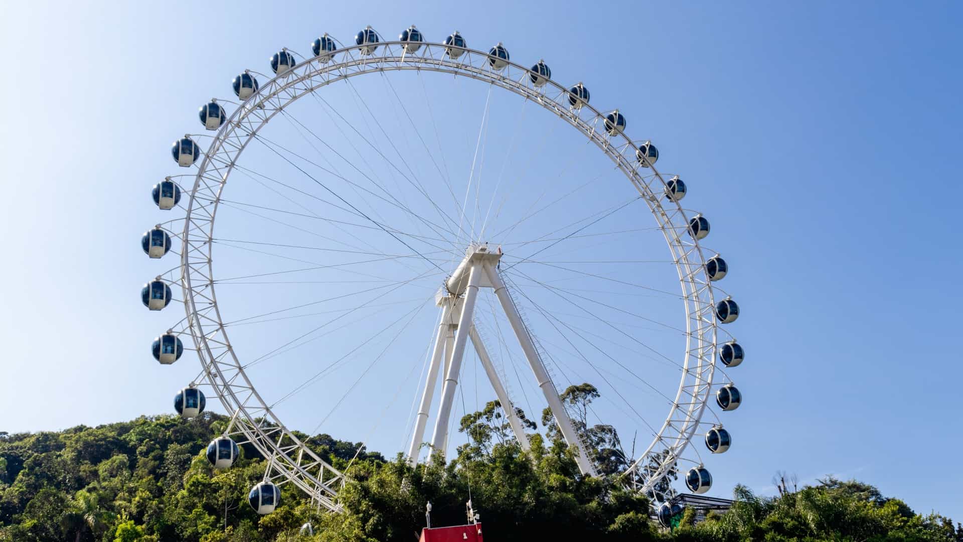 The FG Big Wheel, a massive observation Ferris wheel, stands prominently on the waterfront in Balneário Camboriú, Santa Catarina (SC), Brazil. The image showcases the wheel against the backdrop of the city's densely packed skyline and the ocean.