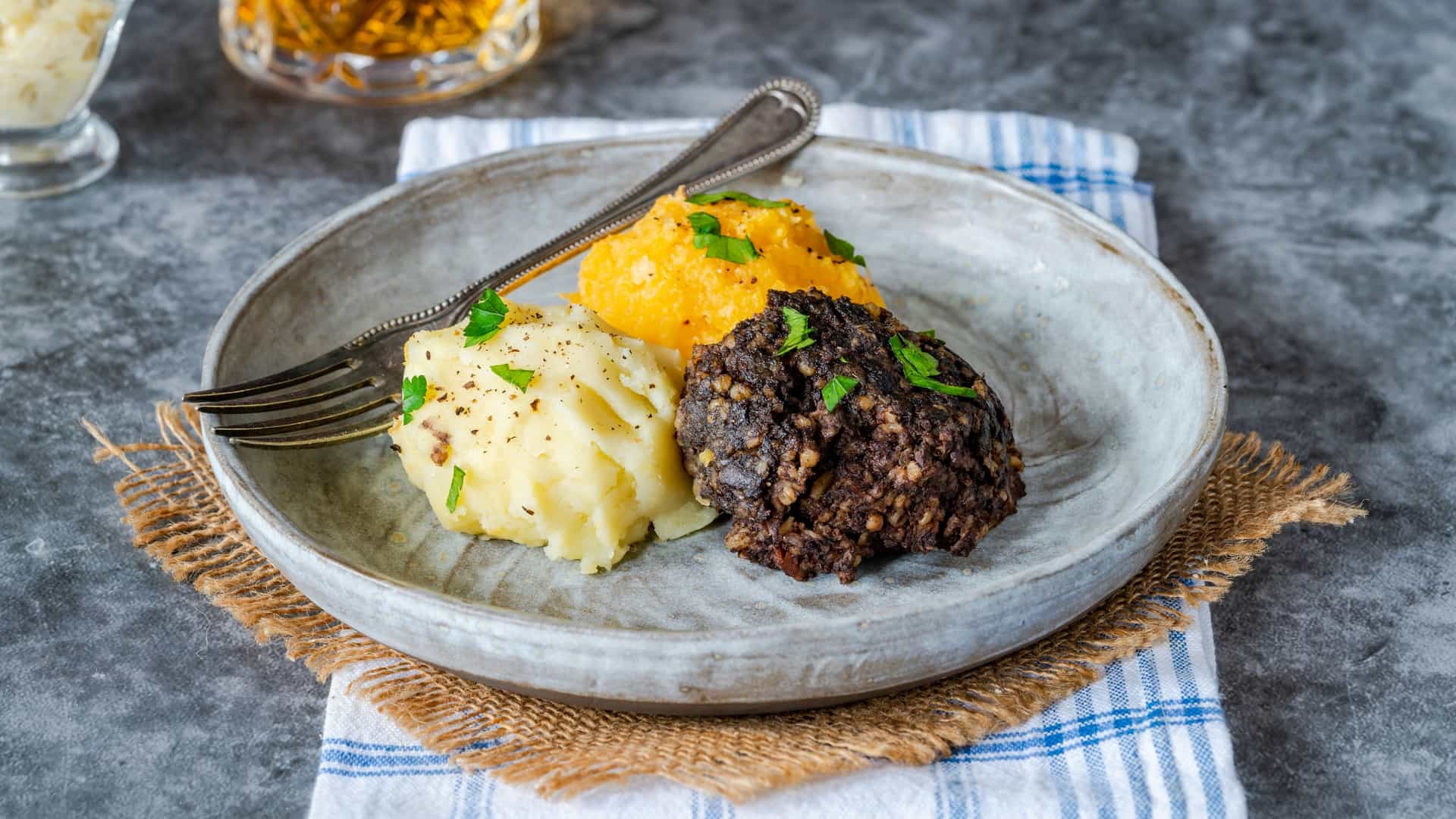 A generous serving of the traditional Scottish national dish, Haggis, Neeps (mashed turnip or swede), and Tatties (mashed potatoes), meticulously plated in three separate mounds, often accompanied by gravy and a wee dram of whisky for a hearty, savory comfort food meal, especially on Burns Night.