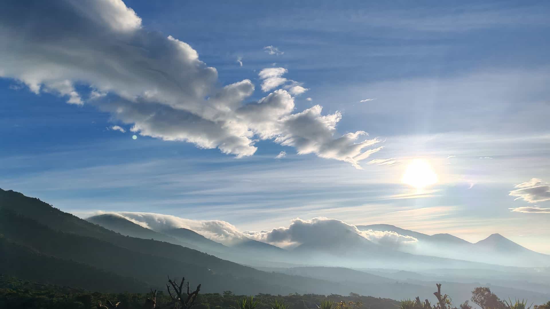 A vibrant sunrise illuminates a breathtaking landscape of layered, tropical mountains in El Salvador, with mist filling the valleys and the sky displaying rich hues of yellow and orange.