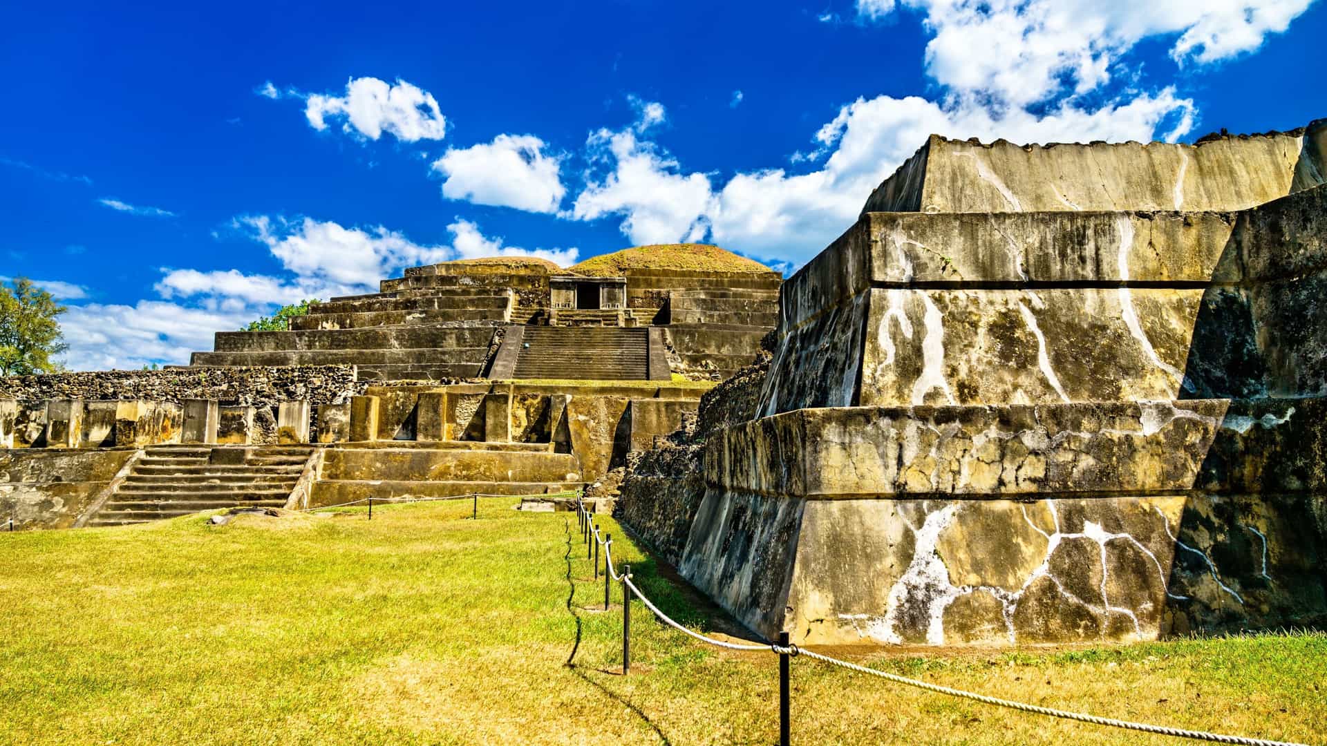 The grand step-pyramid structure of the El Tazumal Mayan ruins near Santa Ana, El Salvador, stands under a sunny sky, representing one of the most important pre-Columbian archaeological sites in the country.