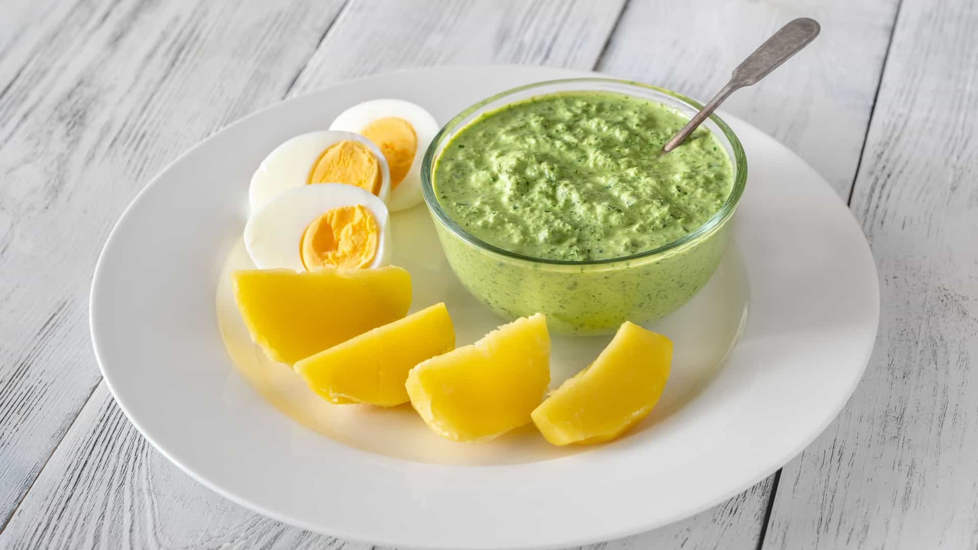 A plate of traditional Frankfurt Green Sauce (Frankfurter Grüne Soße), garnished with fresh herbs and served with halved boiled potatoes and hard-boiled eggs.