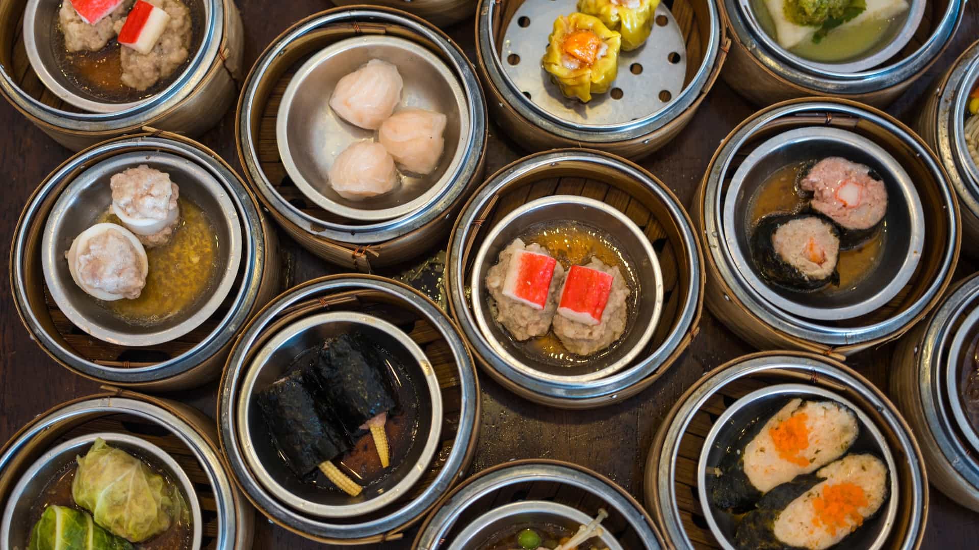  An assortment of various dim sum dishes arranged on a table. The image shows several types of dumplings, including har gow (translucent shrimp dumplings) and siu mai (open topped pork and shrimp dumplings). Other dishes, such as steamed buns or spring rolls, may also be present, all ready to be eaten.