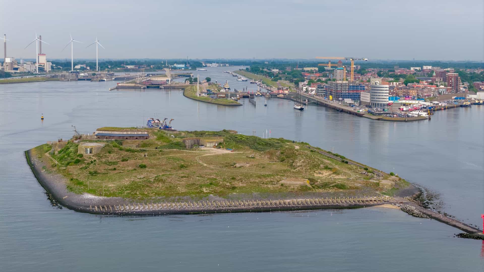 An aerial drone photo of Forteiland (Fort Island), a historic sea fort and UNESCO World Heritage site in the harbor of IJmuiden, Netherlands. The image captures the fort's circular layout, surrounded by the North Sea water, with details of its extensive defense structures and bunkers visible on the island.