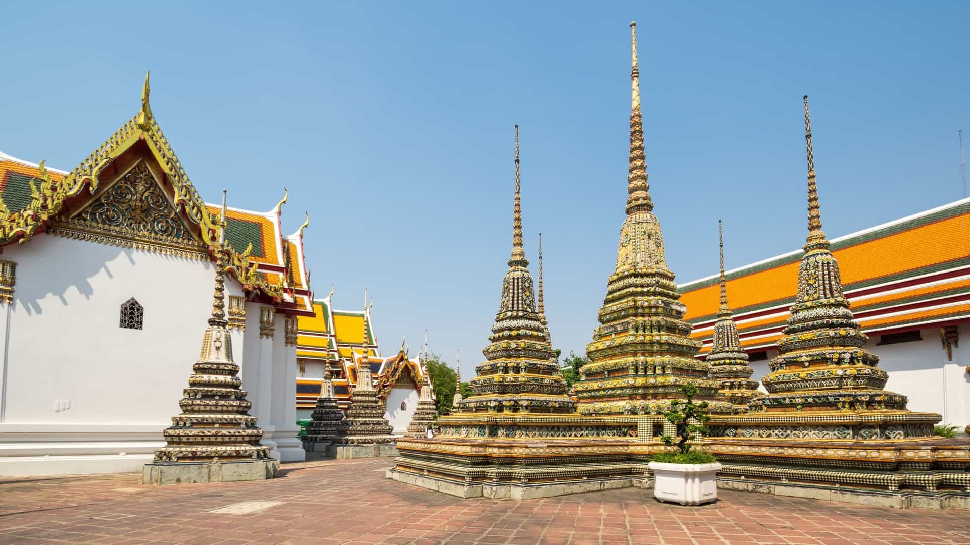 A view of Wat Pho, the Temple of the Reclining Buddha, in Bangkok, Thailand. The focus is on the temple's iconic, massive, gold-plated Reclining Buddha statue, which is 46 meters long and 15 meters high. The image captures the serene yet immense scale of the Buddha, possibly showing the ornate mother-of-pearl inlaid soles of the feet or the golden body, surrounded by the interior of the temple hall.