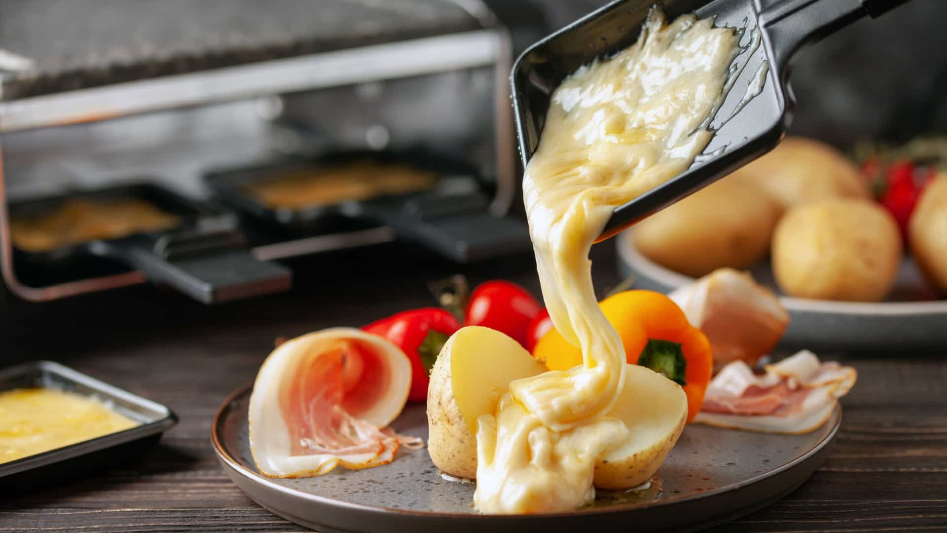 A close-up shot of traditional Swiss raclette cheese being melted, likely using a special raclette machine or heating element. The surface of the pale yellow, semi-hard cheese is bubbly, soft, and visibly molten, ready to be scraped off. The melted cheese is typically a rich, creamy, and savory delight.