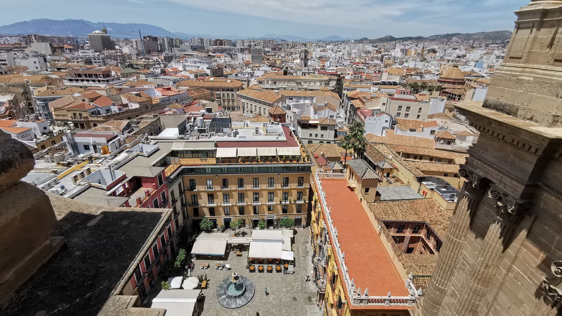 Aerial panoramic view of the historic center of Málaga, Spain, highlighting the massive Renaissance structure of the Malaga Cathedral and the ancient Alcazaba fortress among a dense, white cityscape extending toward the Mediterranean Sea.