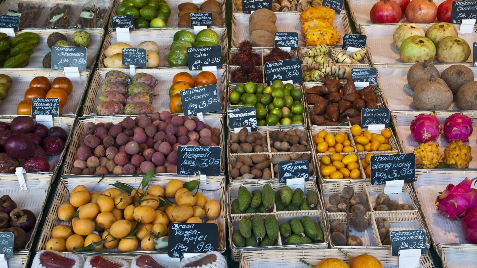 An abundance of colorful fresh fruits and produce, including melons, berries, and citrus, displayed at a market stall at the vibrant Viktualienmarkt in Munich, Germany.