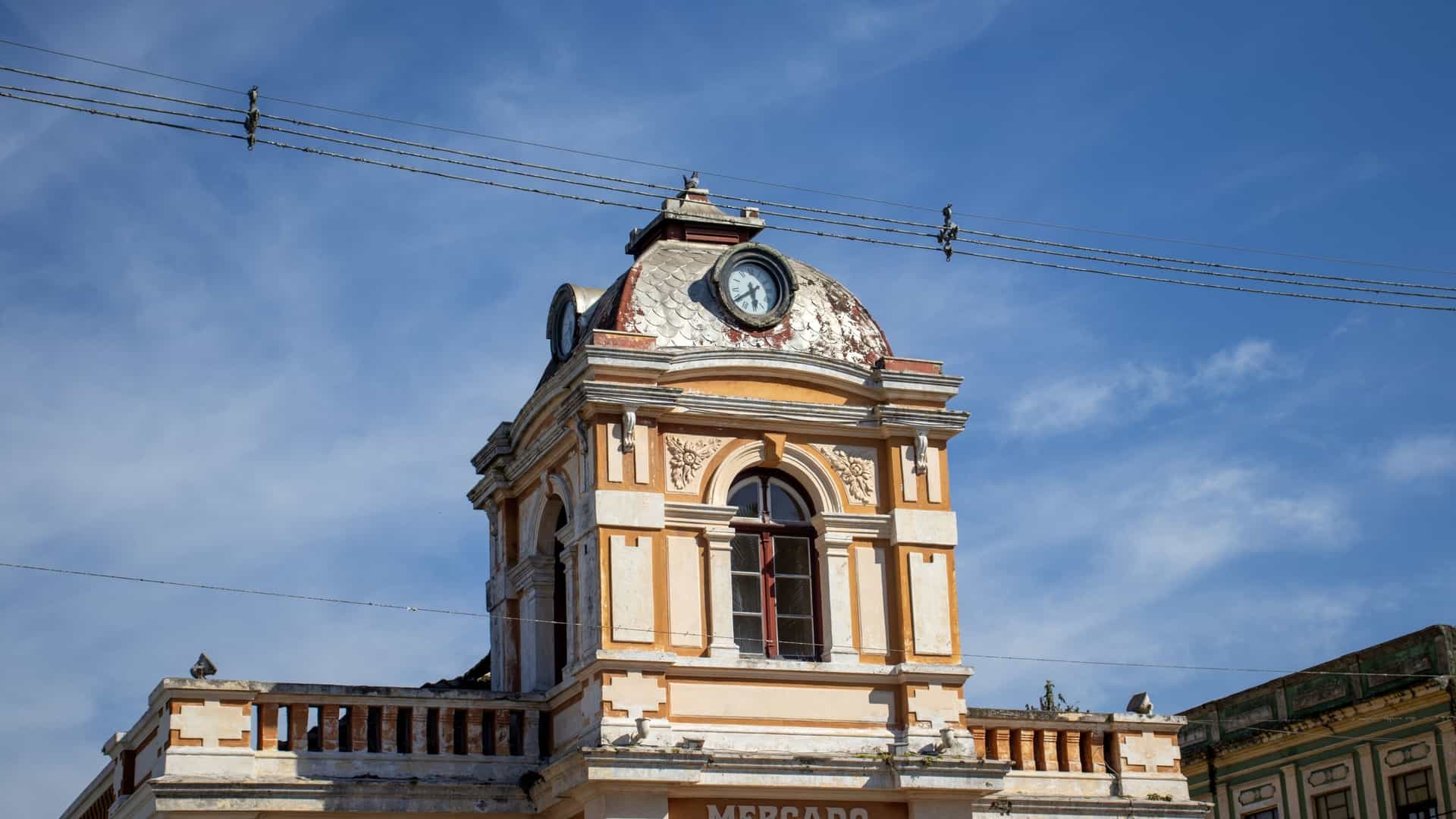 A street view in the historic center of a city in Paraná, Brazil, where a large, skeletal modern construction site of a high-rise building is visible behind and towering over older, lower-rise architecture. The old buildings in the foreground are historic, two- or three-story structures, indicating the contrast between preservation and urban development.