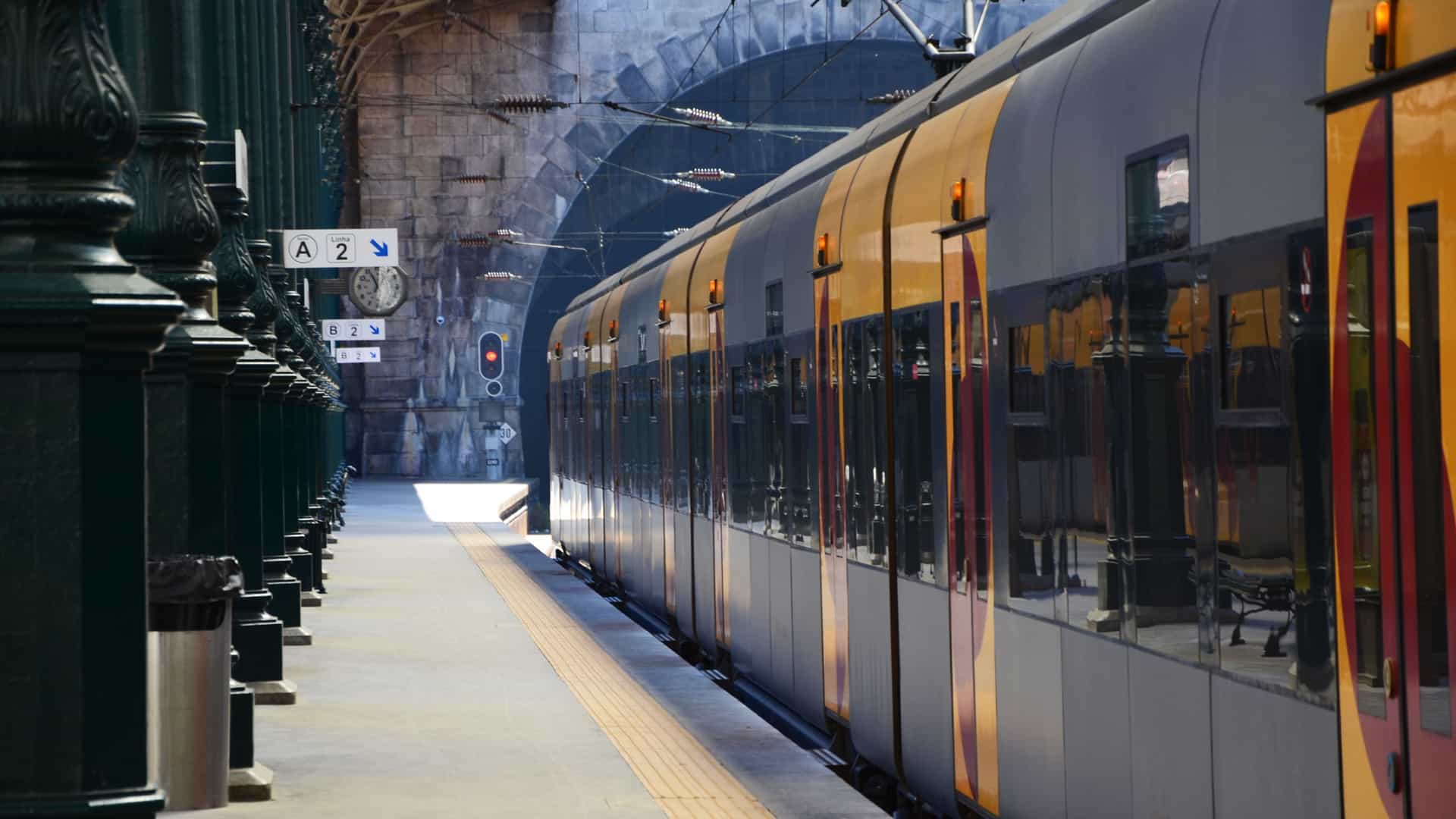 Interior view of São Bento Station in Porto, Portugal, showing a modern train parked at the platform beneath the historic, vaulted iron and glass arched roof of the train shed.