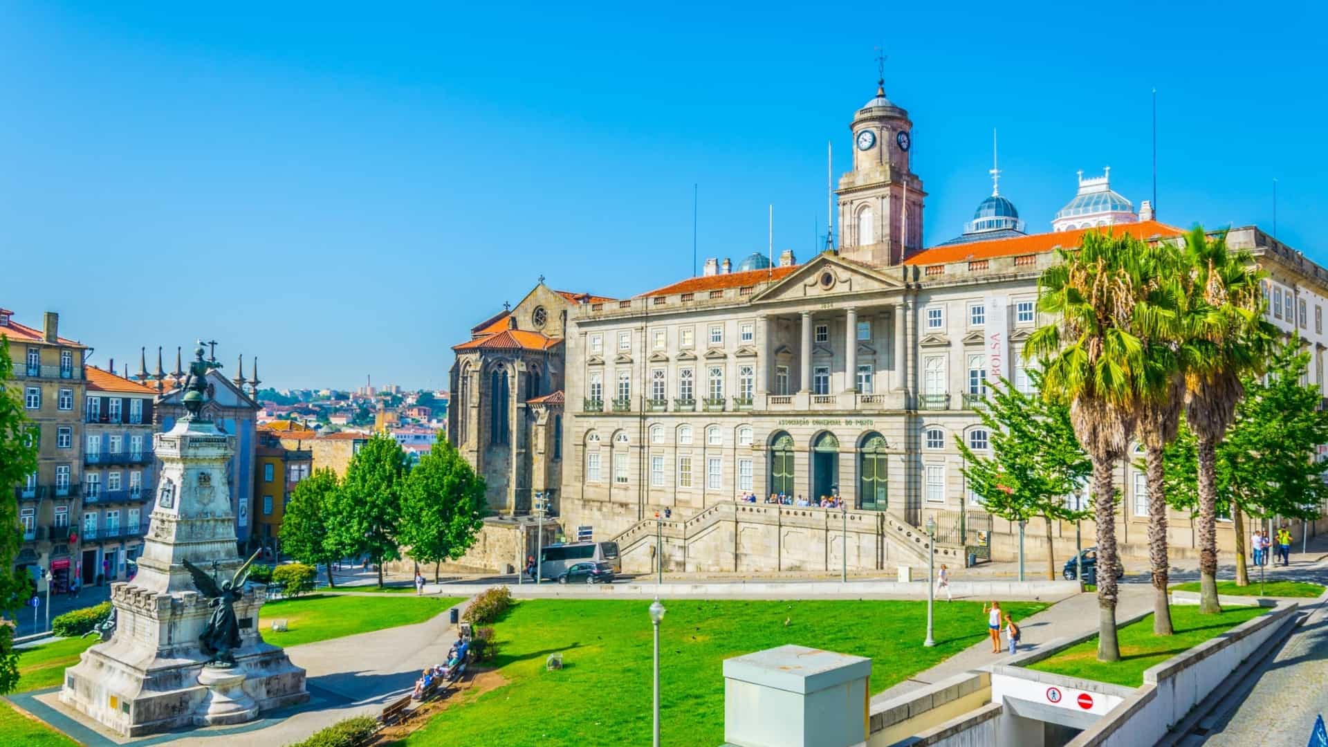 The grand Neoclassical exterior and facade of the Palácio da Bolsa (Stock Exchange Palace) in Porto, Portugal. The historic building, a UNESCO World Heritage Site, stands prominently against a blue sky, viewed from the public square.