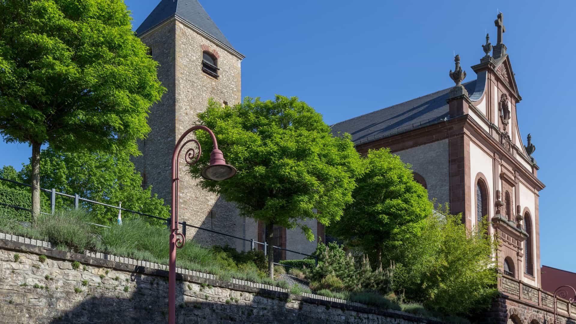 The Parish Church of Saint Laurentius and Saint Stephanus in Remich, Luxembourg, featuring its distinctive, robust medieval tower built on Roman foundations, attached to the main body of the church.