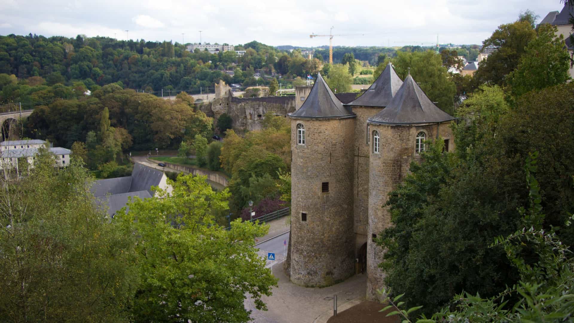 A wide view of Schengen Castle in Luxembourg, showing the pale, 19th-century manor house structure built upon the foundation of the former fortified castle, with the medieval round tower still standing prominently on the left.