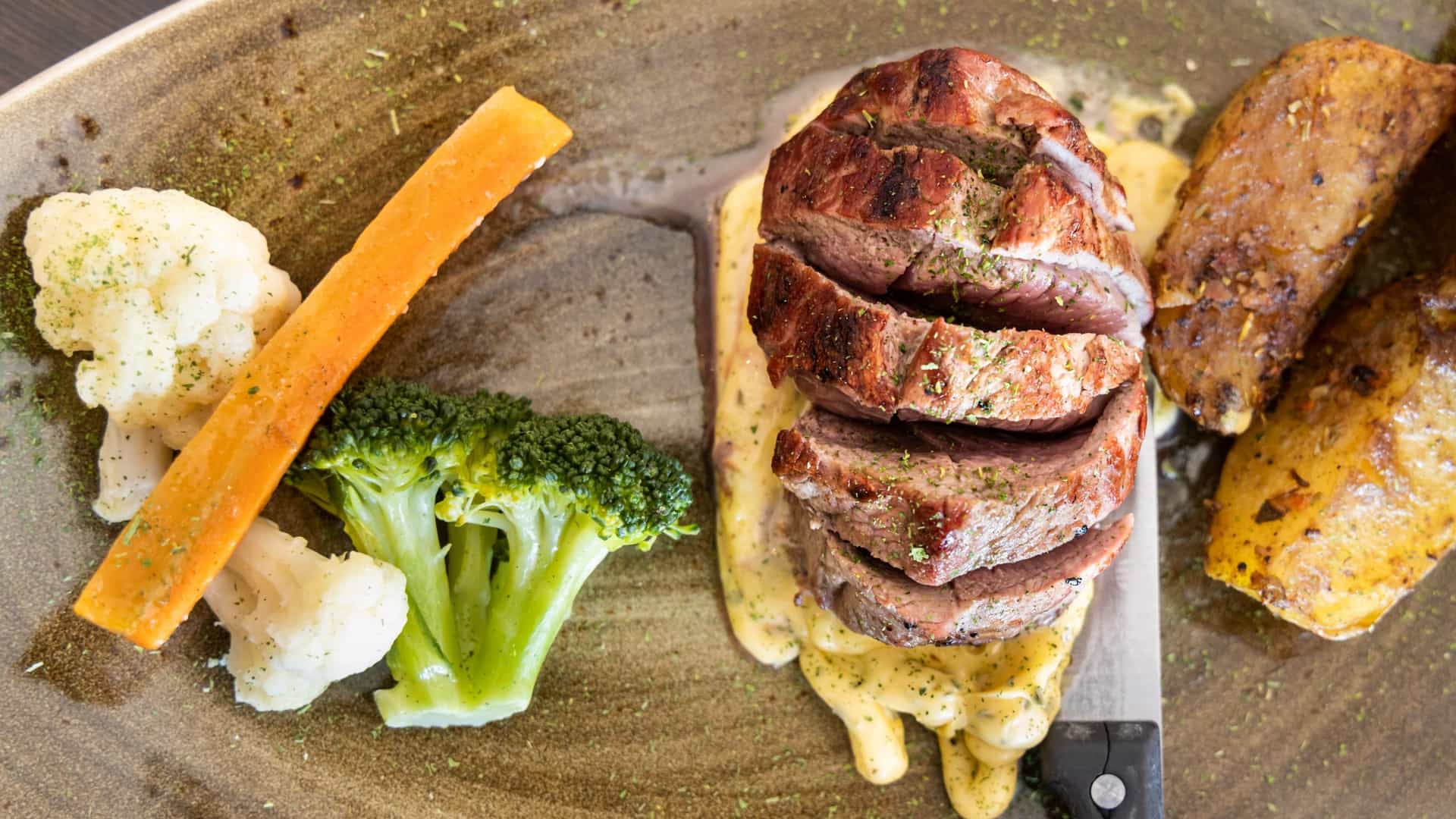  A close up of a serving of traditional Icelandic roast lamb, sliced and plated. The tender, roasted lamb meat is accompanied by a white side dish, typically mashed or boiled potatoes, and a portion of bright green vegetables, likely green peas or beans.