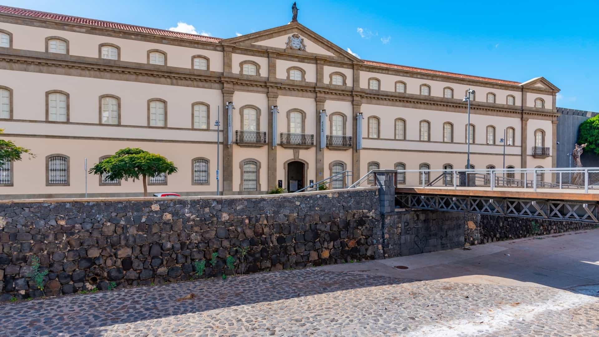  The neoclassical facade of the Museum of Nature and Archaeology (MUNA) in Santa Cruz de Tenerife, housed in the historic Antiguo Hospital Civil building. The large, light colored stone building features a grand entrance with tall columns and is a cultural heritage site in the Canary Islands.