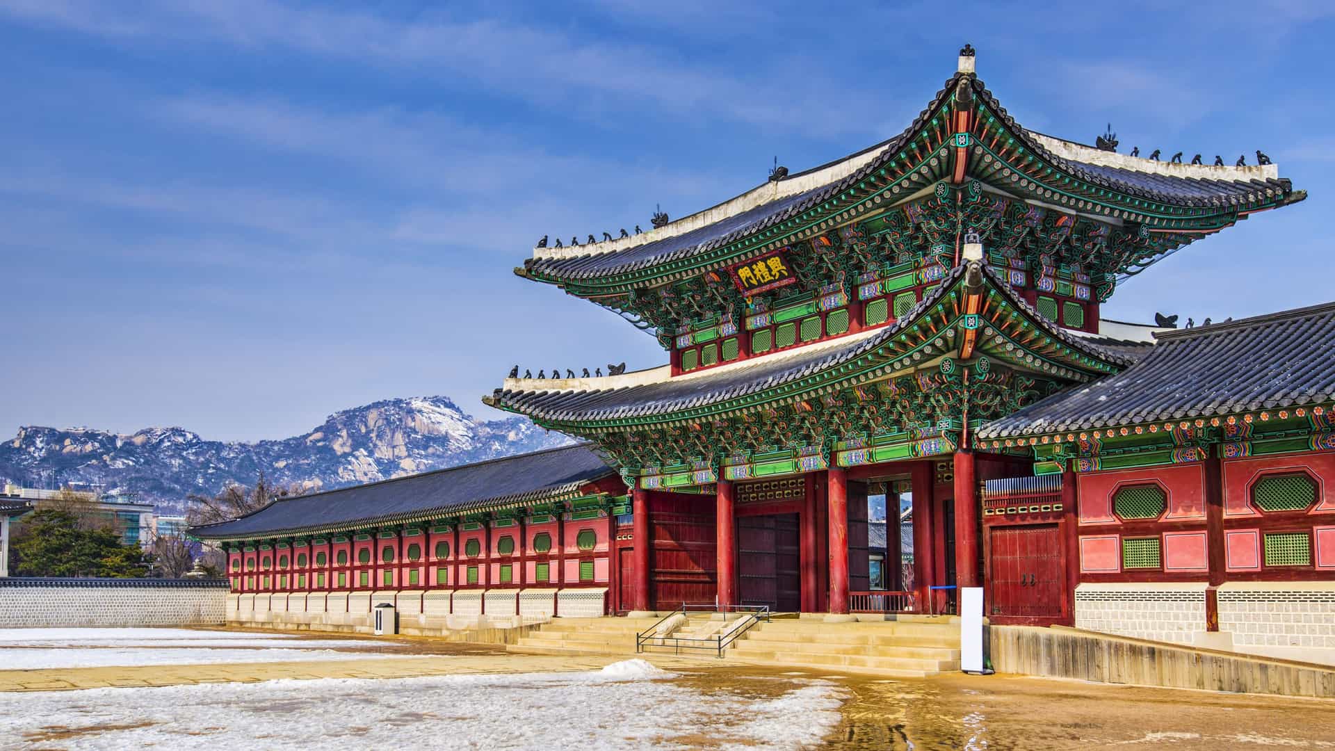 A traditional Korean palace building on the grounds of Gyeongbokgung Palace in Seoul, South Korea. The wooden structure features a curved, tiled roof and intricate, colorful Dancheong (traditional Korean paintwork) under the eaves, set against a backdrop of a clear sky and surrounding grounds.
